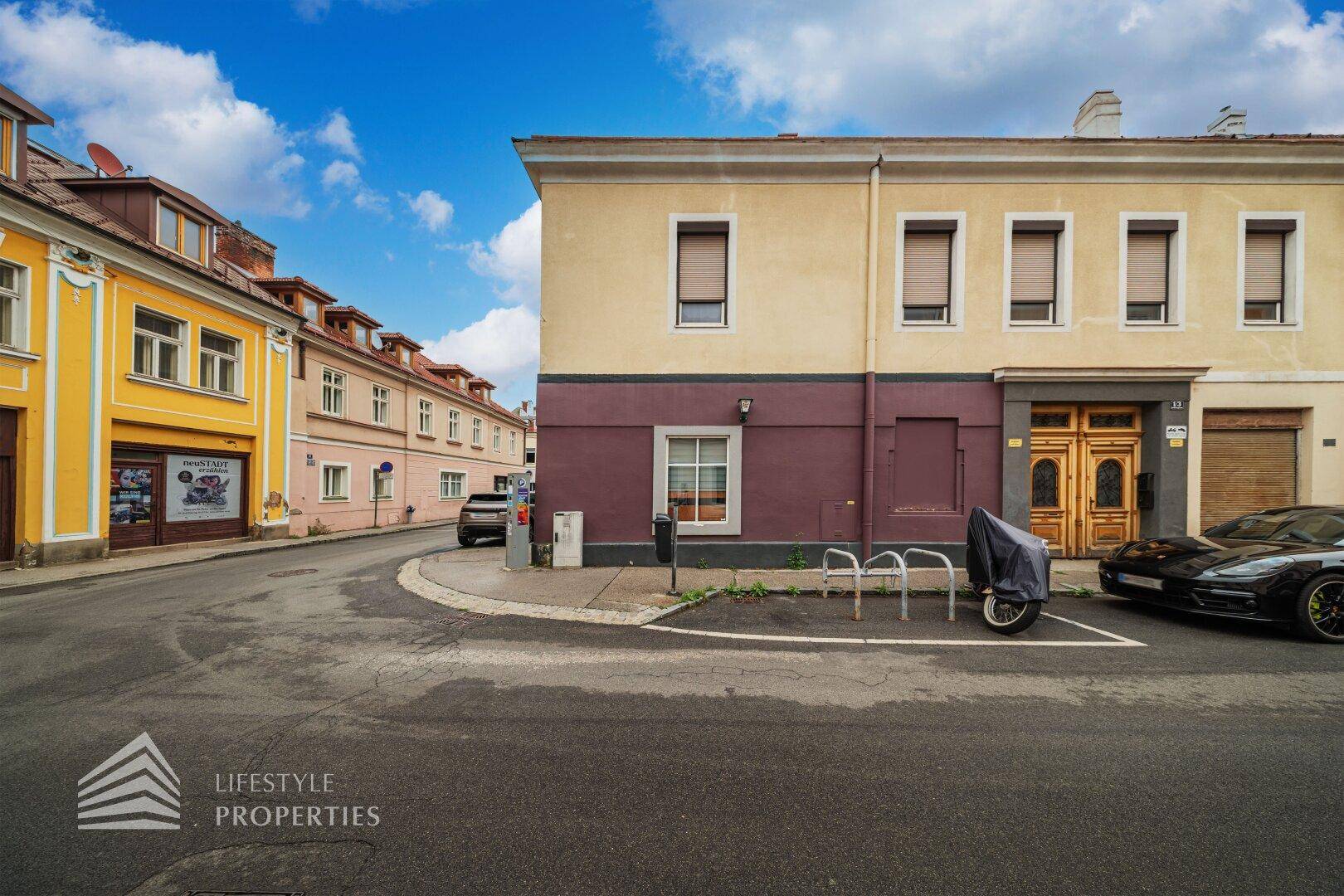 Ansicht eines Gebäudes an einer Straßenecke mit geparkten Autos und einem blauen Himmel.