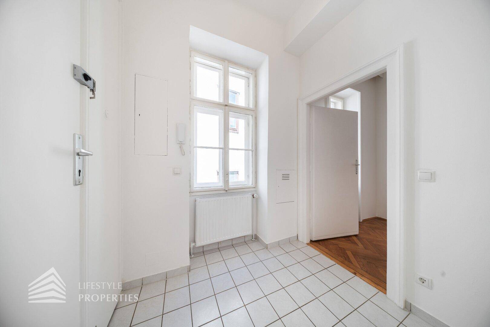 Eingangsbereich mit hellen Fliesen, einem Fenster und Zugang zu weiteren Räumen.