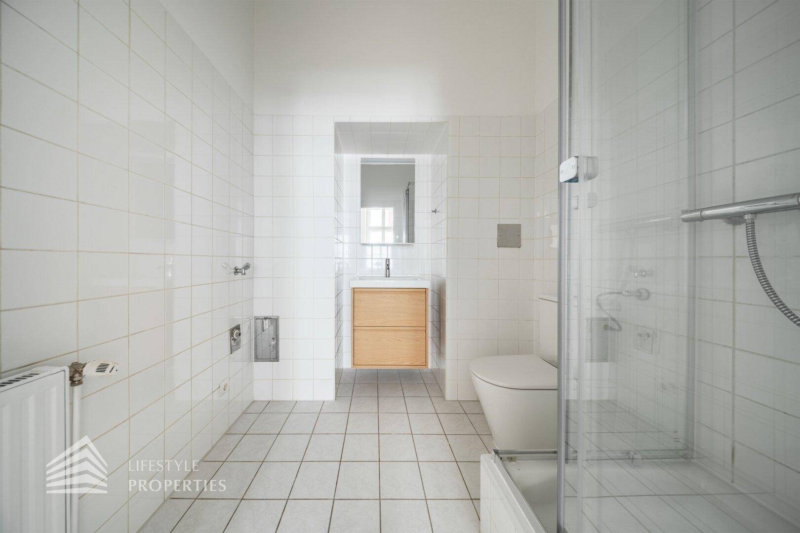 Modernes Badezimmer mit weißen Fliesen, Duschkabine und Holzwaschtisch.