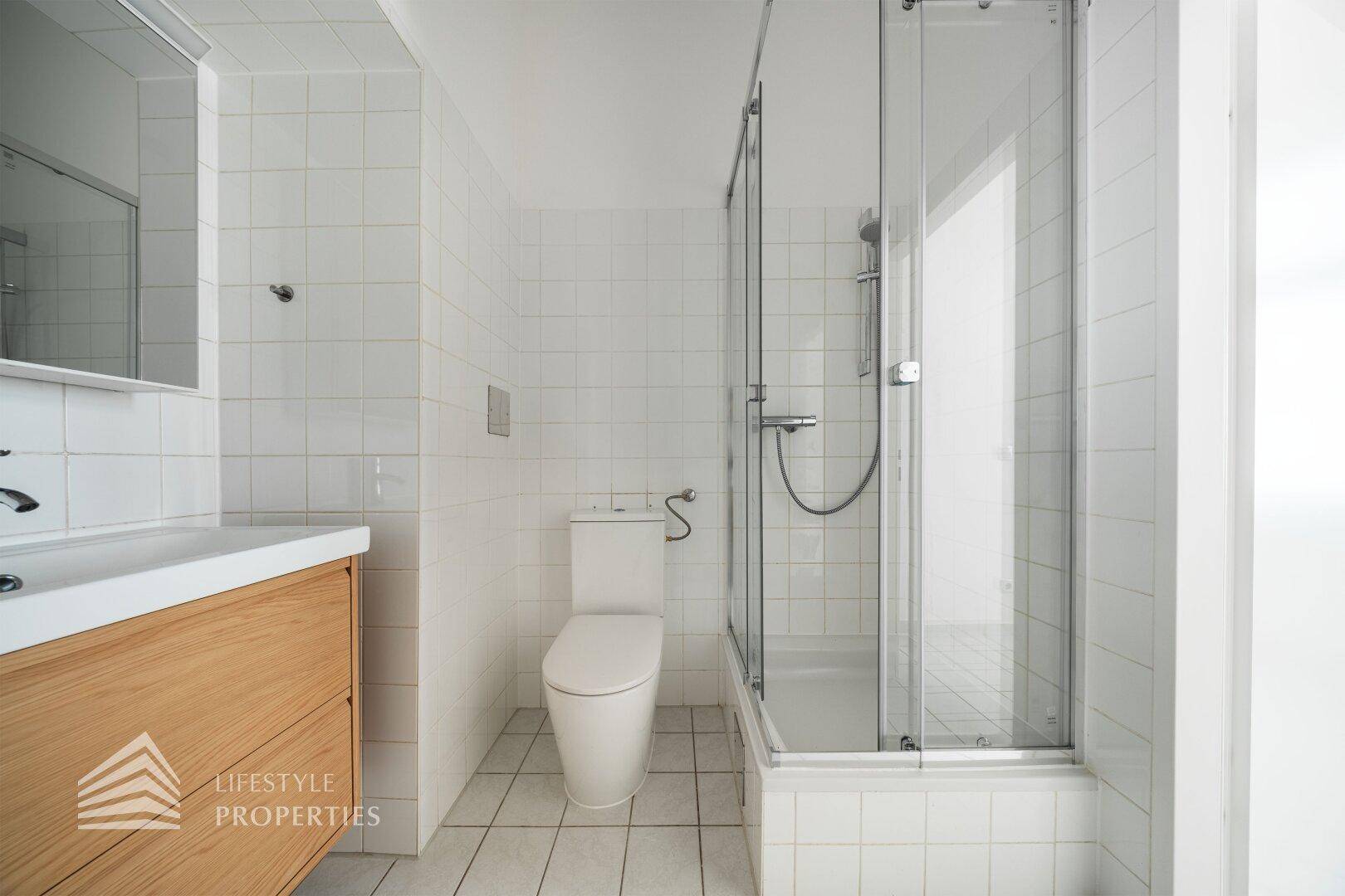 Helles Badezimmer mit Duschkabine, WC und einem Waschtisch mit Holzunterschrank.