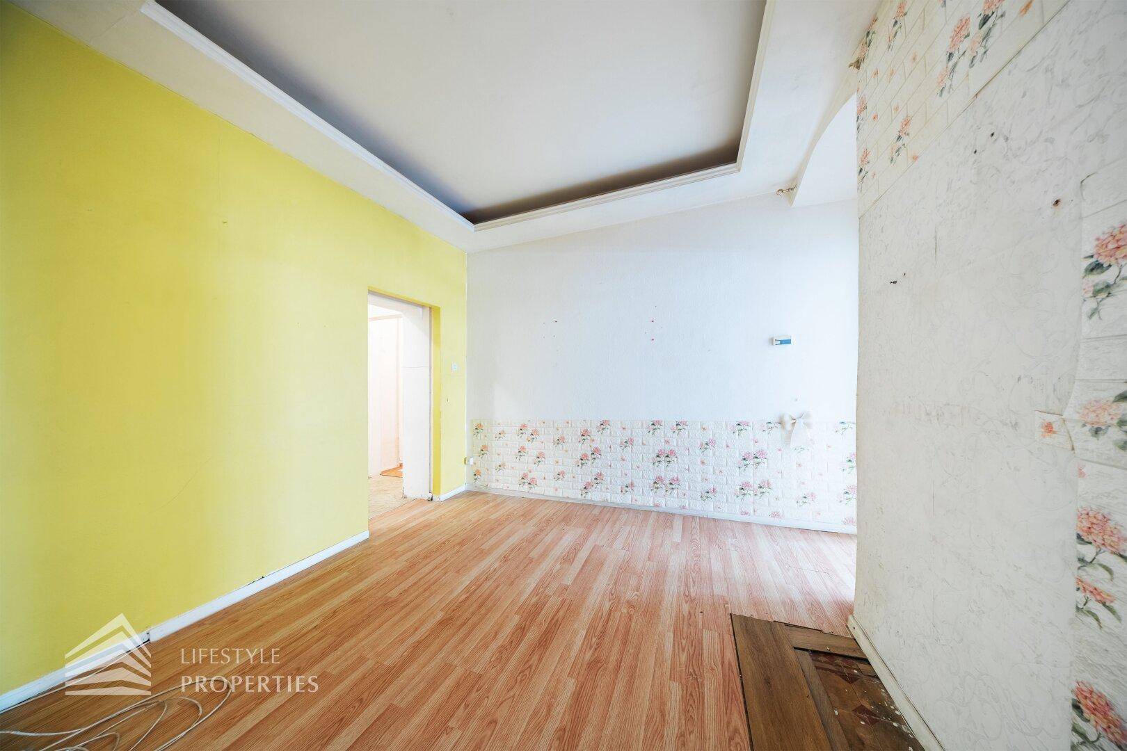 Raum mit gelber Wand, teilweise entfernter Tapete und Laminatboden.