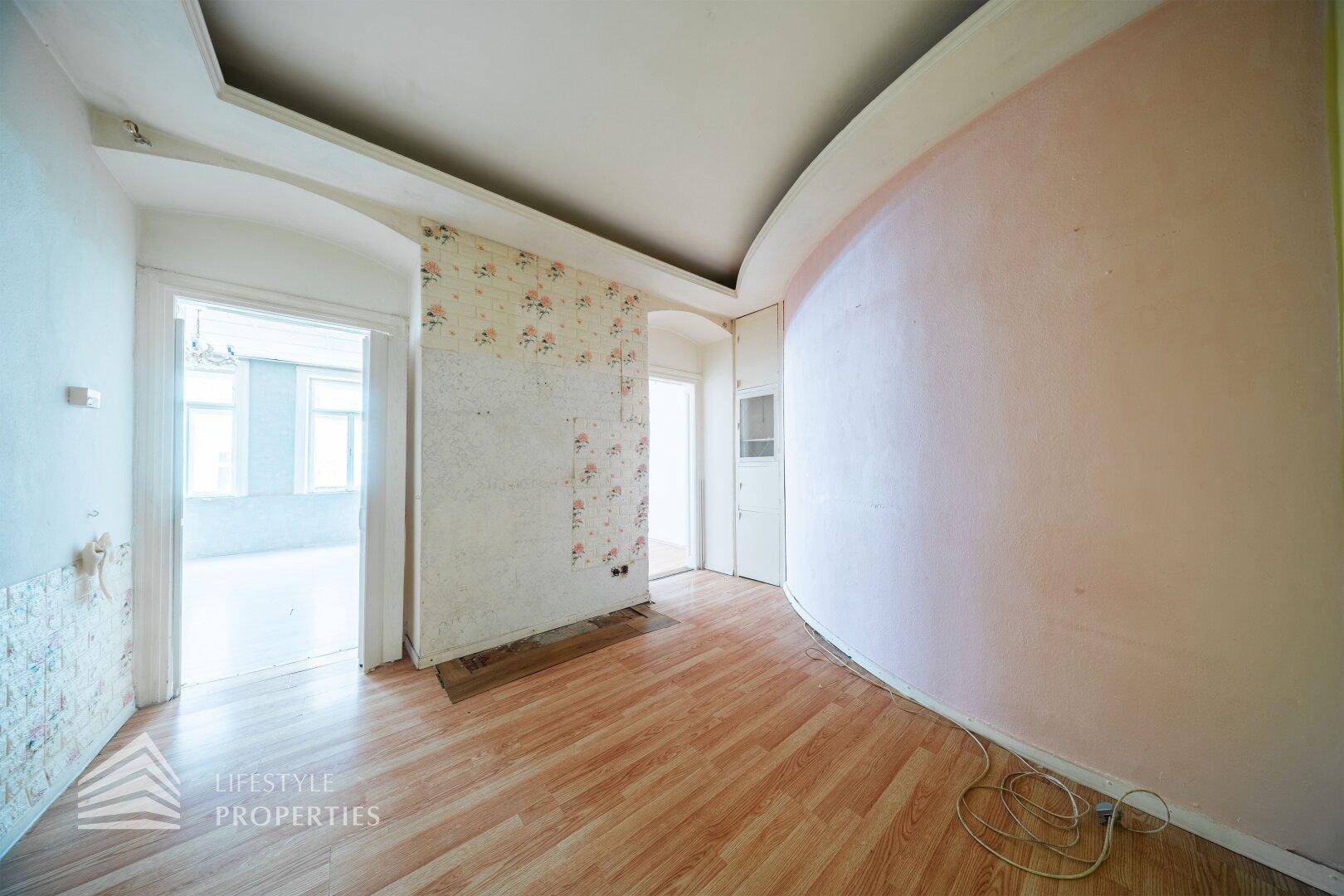 Unmöblierter Raum mit Laminatboden, geschwungener Wand und floraler Tapete.