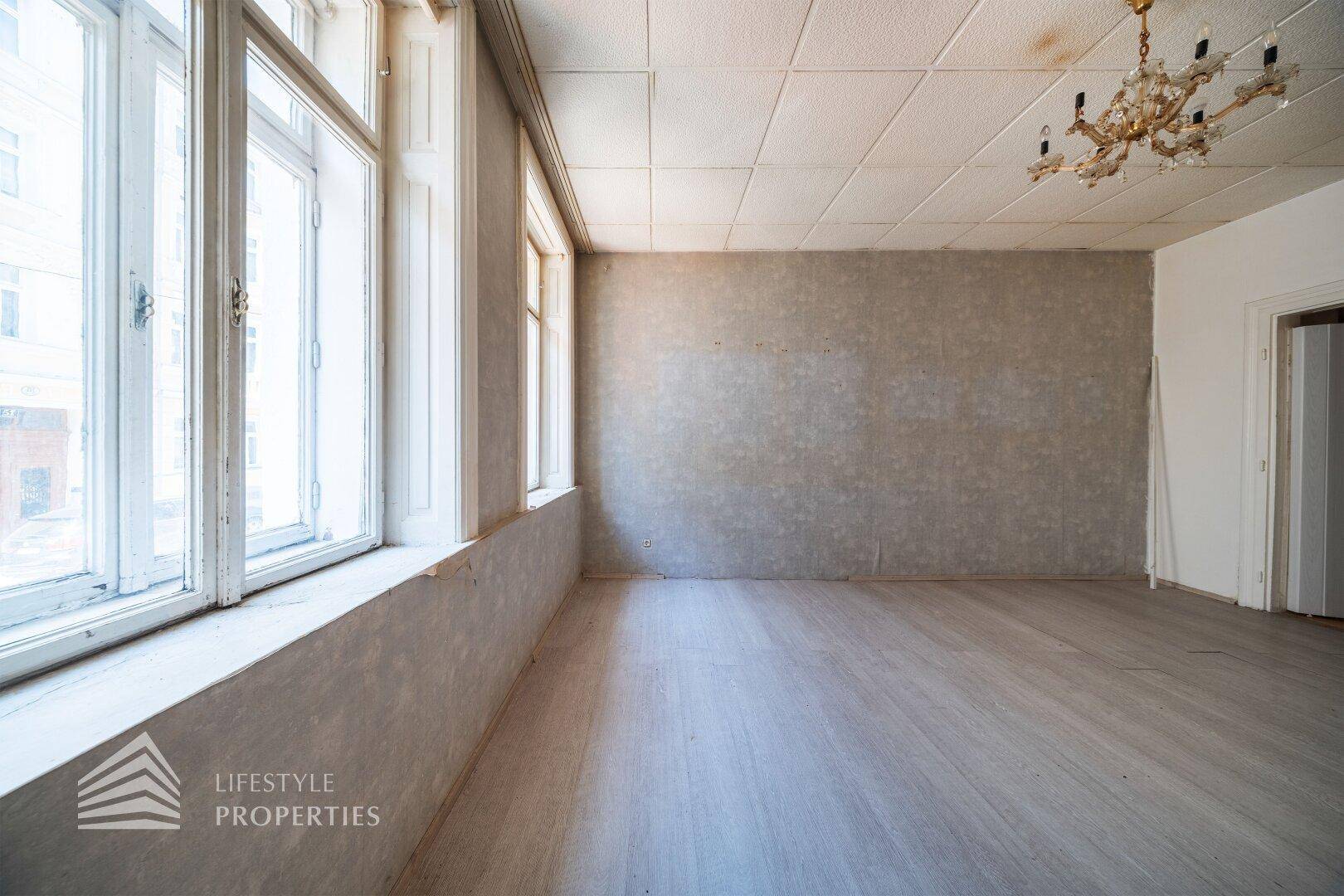 Heller Raum mit mehreren hohen Fenstern, Laminatboden und Kronleuchter.