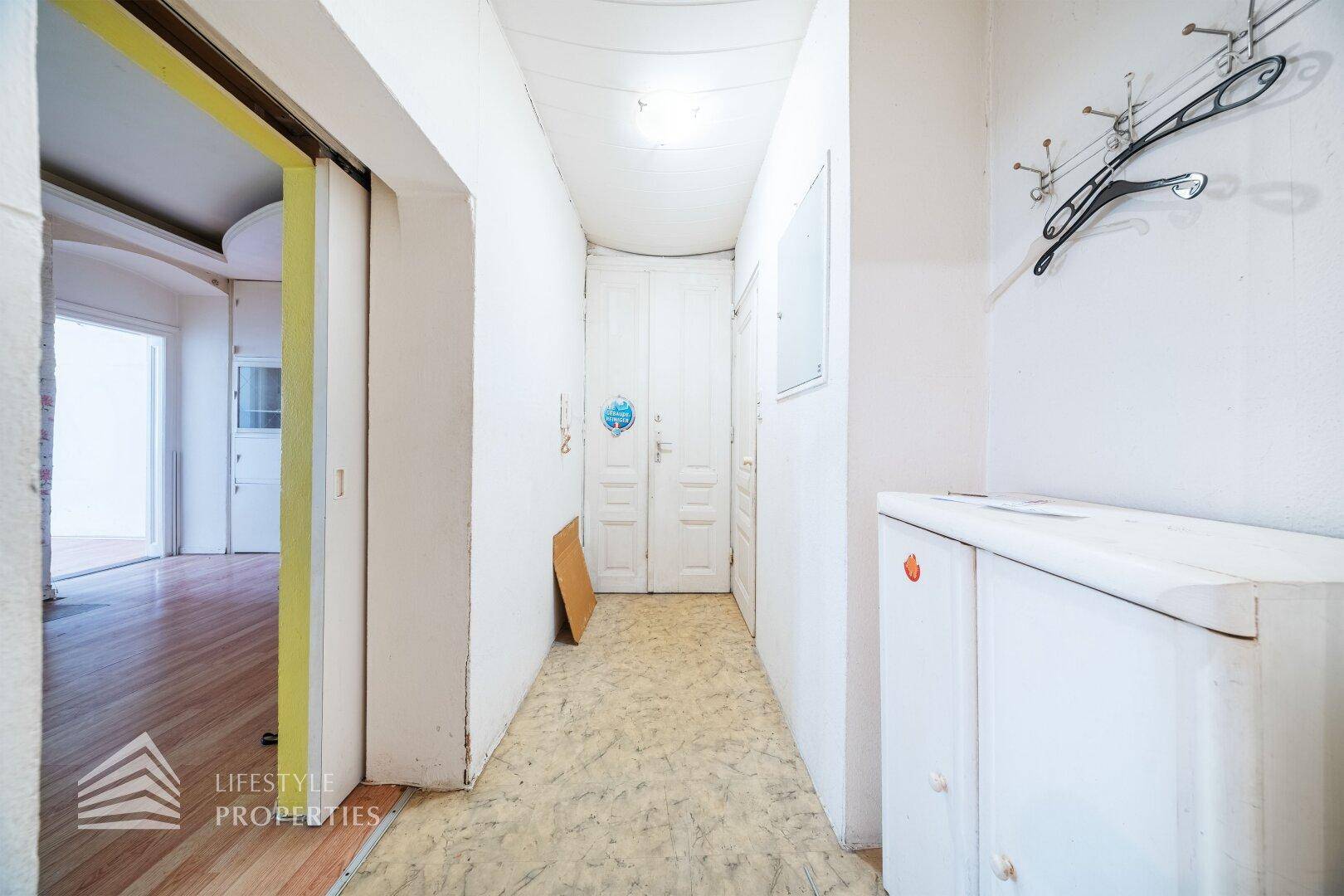 Schmaler Flur mit Linoleumboden, Garderobe und Zugang zu weiteren Räumen.