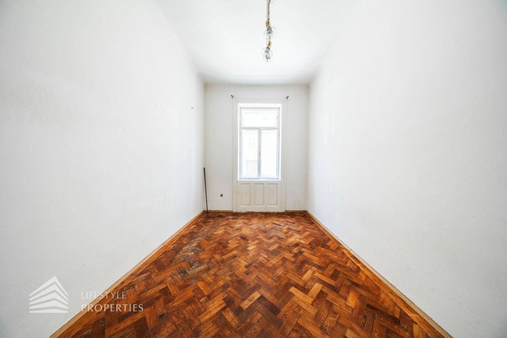 Schmaler Raum mit Fischgrätparkett und einem Fenster, ideal für ein kleines Schlafzimmer oder Büro.
