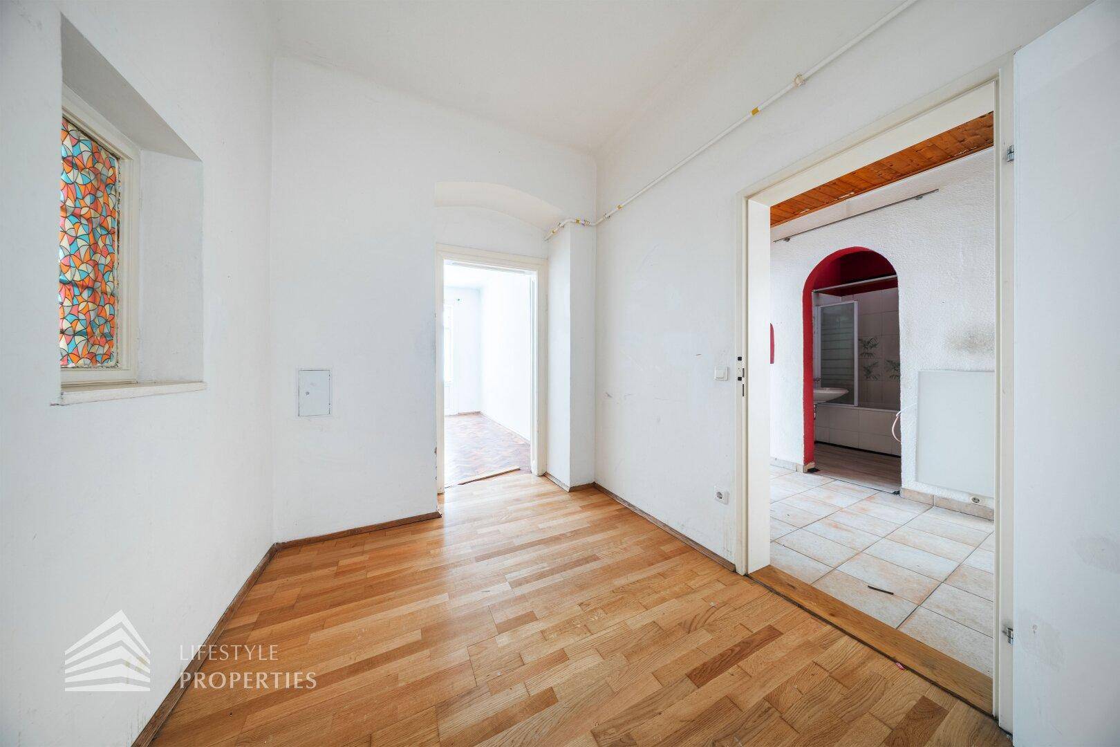Flur mit Holzboden und einem farbigen Glasfenster, verbindet verschiedene Räume der Wohnung.
