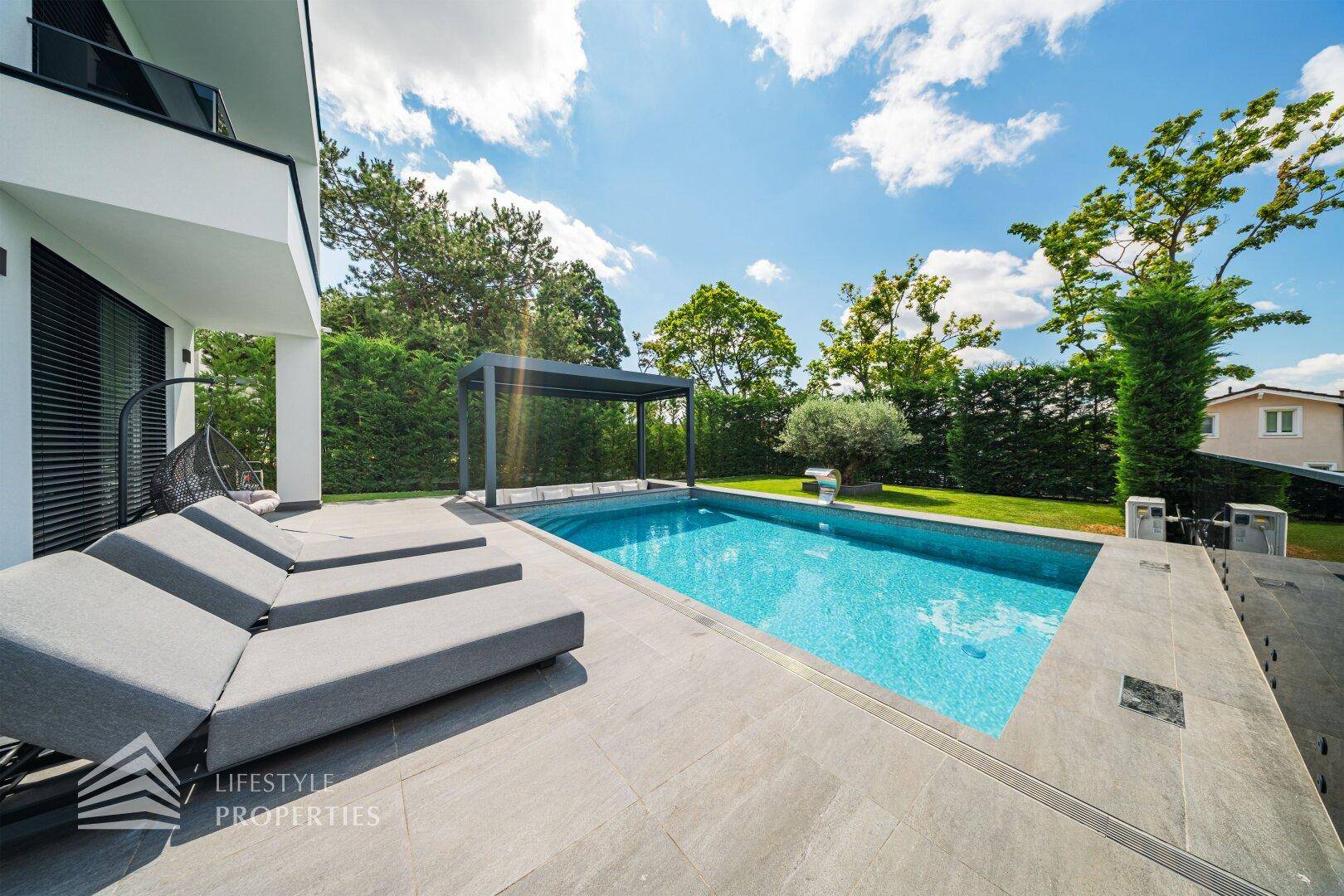 Großzügige Poolterrasse mit bequemen Sonnenliegen und Blick auf den gepflegten Garten.