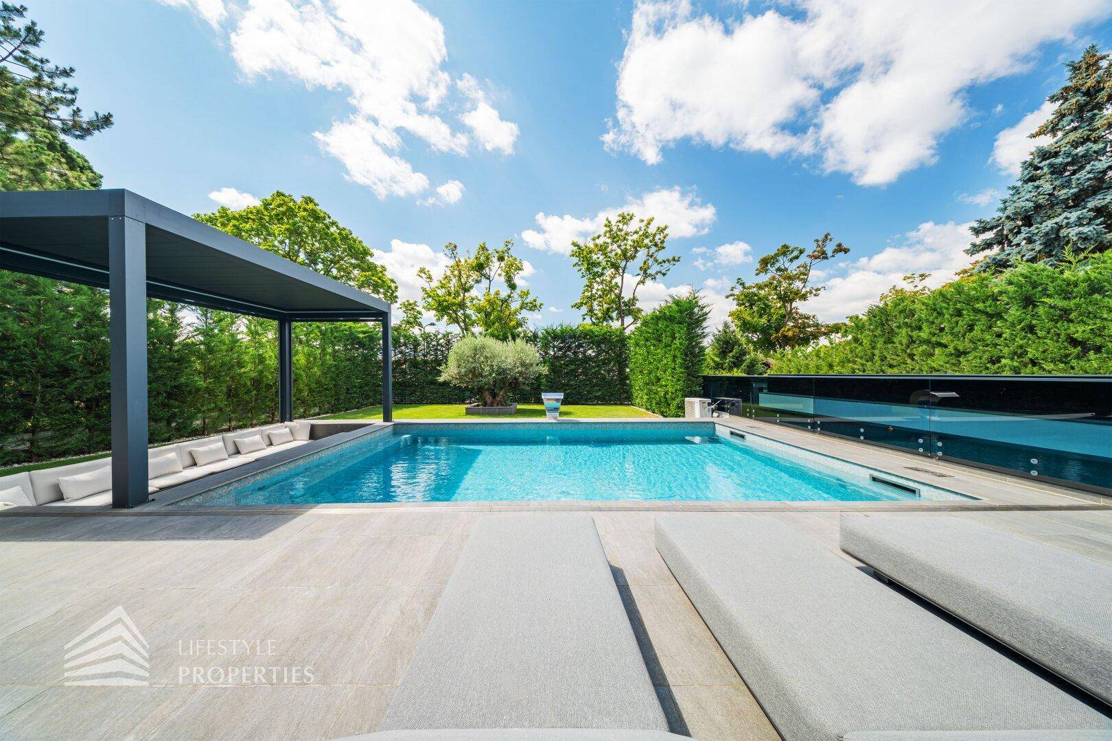 Weitläufiger Poolbereich mit Pergola, eingelassenem Sitzbereich und üppiger grüner Bepflanzung.