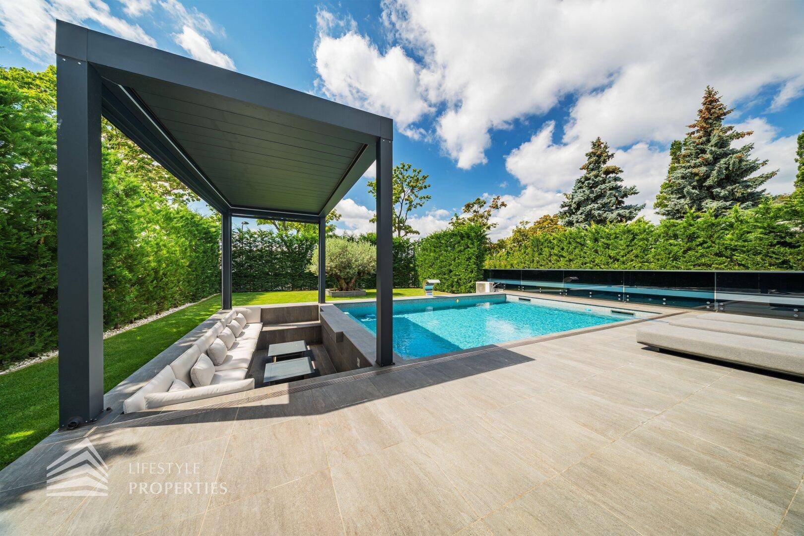 Überdachte Terrasse mit eingelassenem Lounge-Bereich und Blick auf den Pool und den Garten.