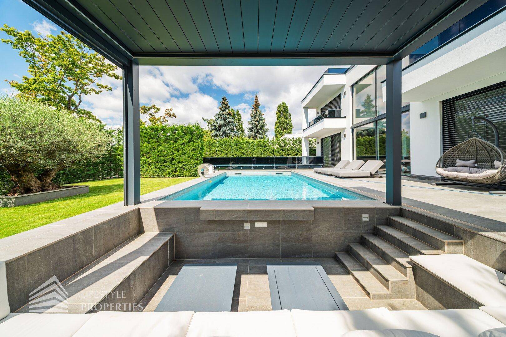 Stilvoller, eingelassener Sitzbereich unter einer Pergola mit direktem Blick auf den Pool und die Villa.