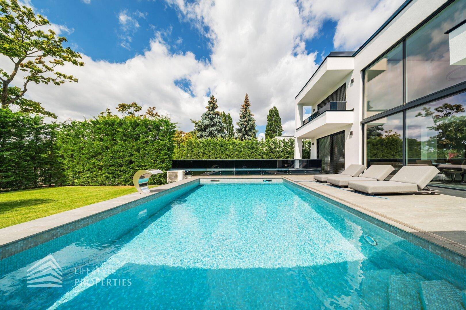 Langer, rechteckiger Pool mit Sonnenliegen und Blick auf die moderne Architektur des Hauses.