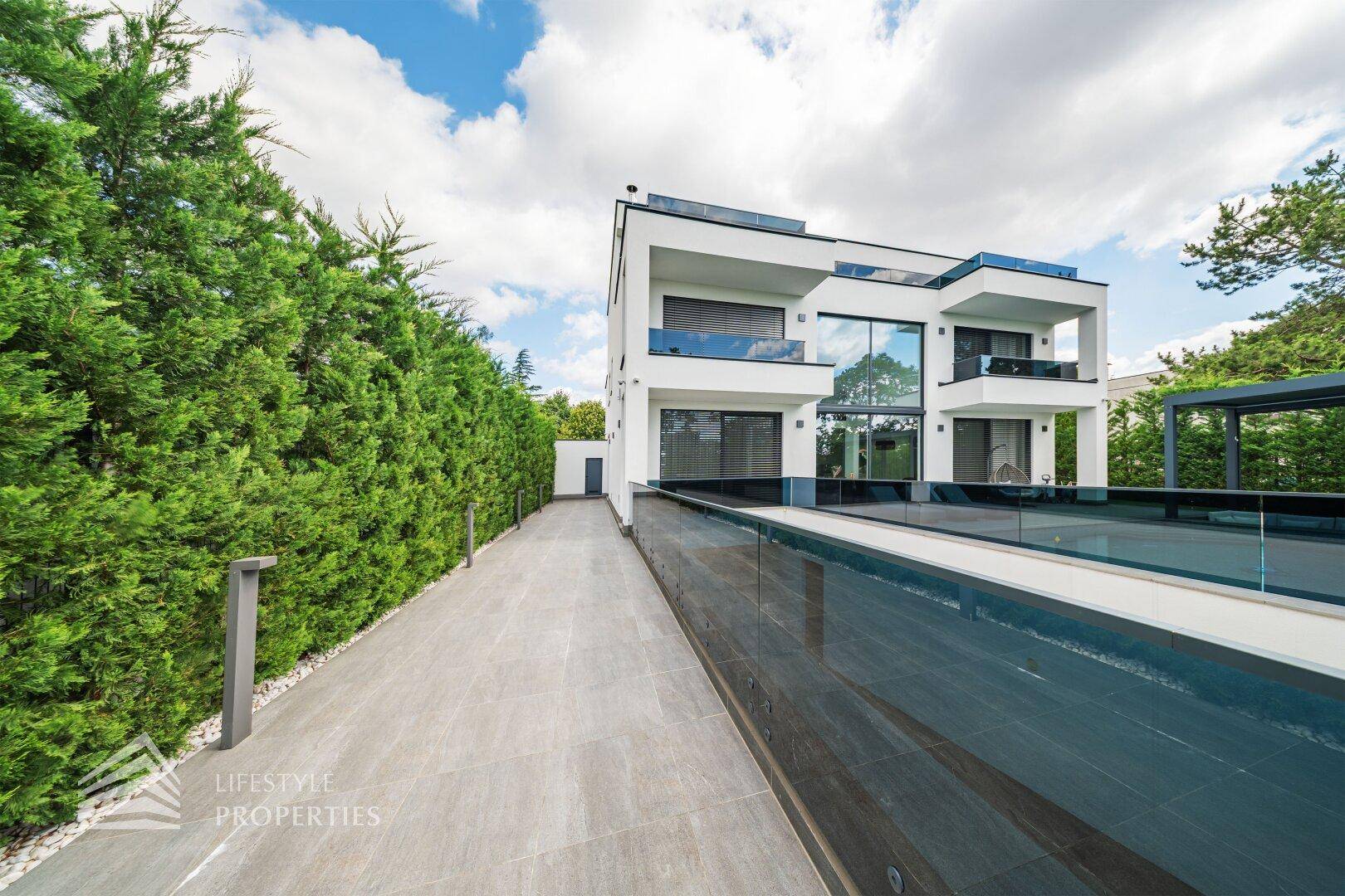 Moderne Villa mit Zufahrt, umgeben von grünen Hecken und einem eleganten Poolbereich.