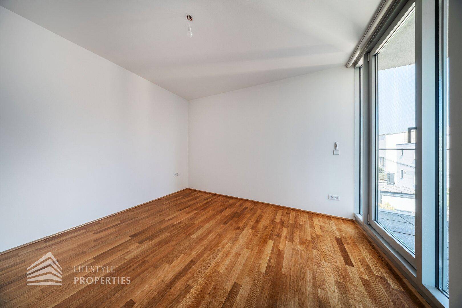 Helles Schlafzimmer mit Holzboden und großen Fenstern, die viel Tageslicht hereinlassen.