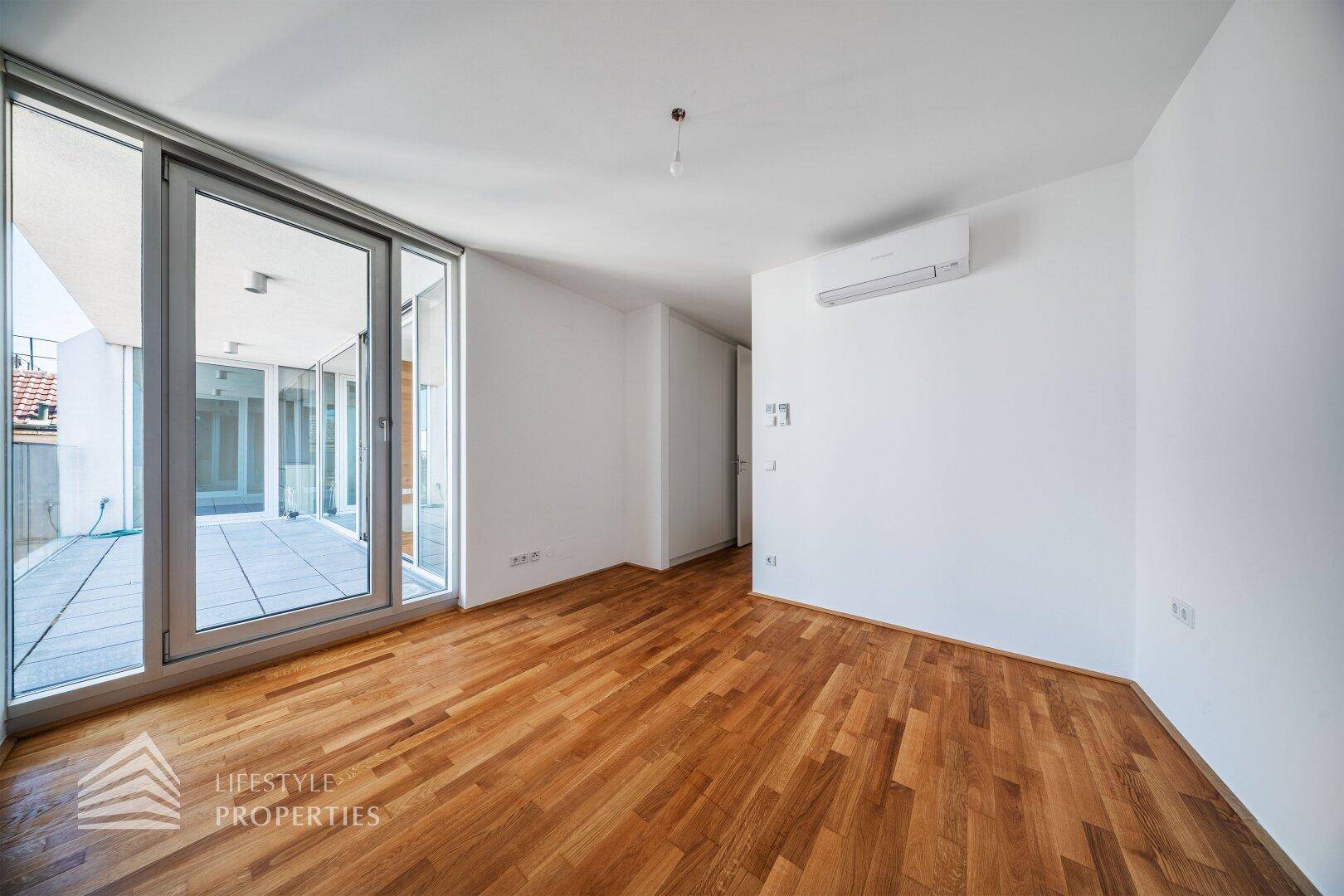 Geräumiges Schlafzimmer mit Holzboden, Klimaanlage und Zugang zu einer Terrasse.