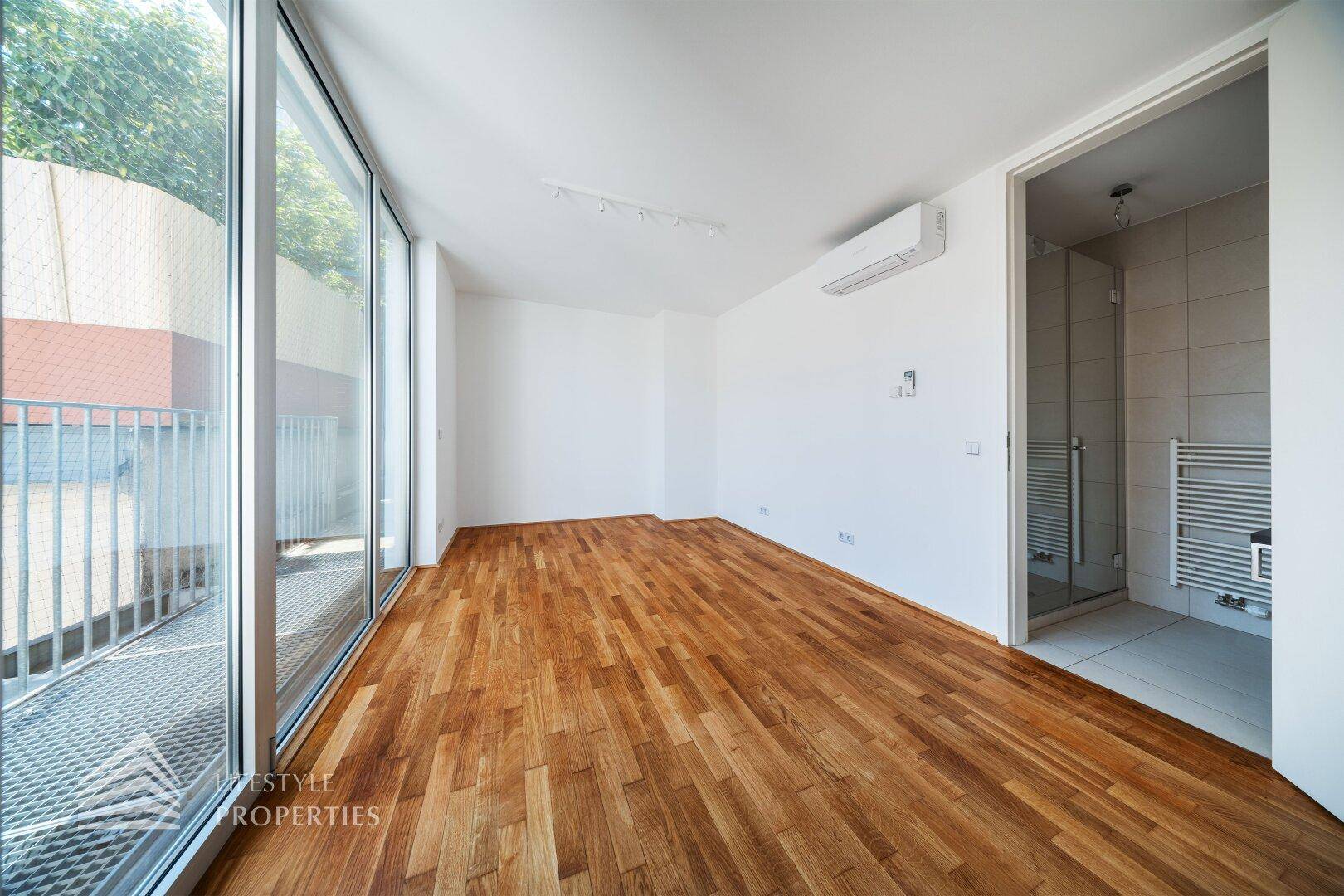 Helles Schlafzimmer mit Holzboden, Klimaanlage und direktem Zugang zu einem Badezimmer.