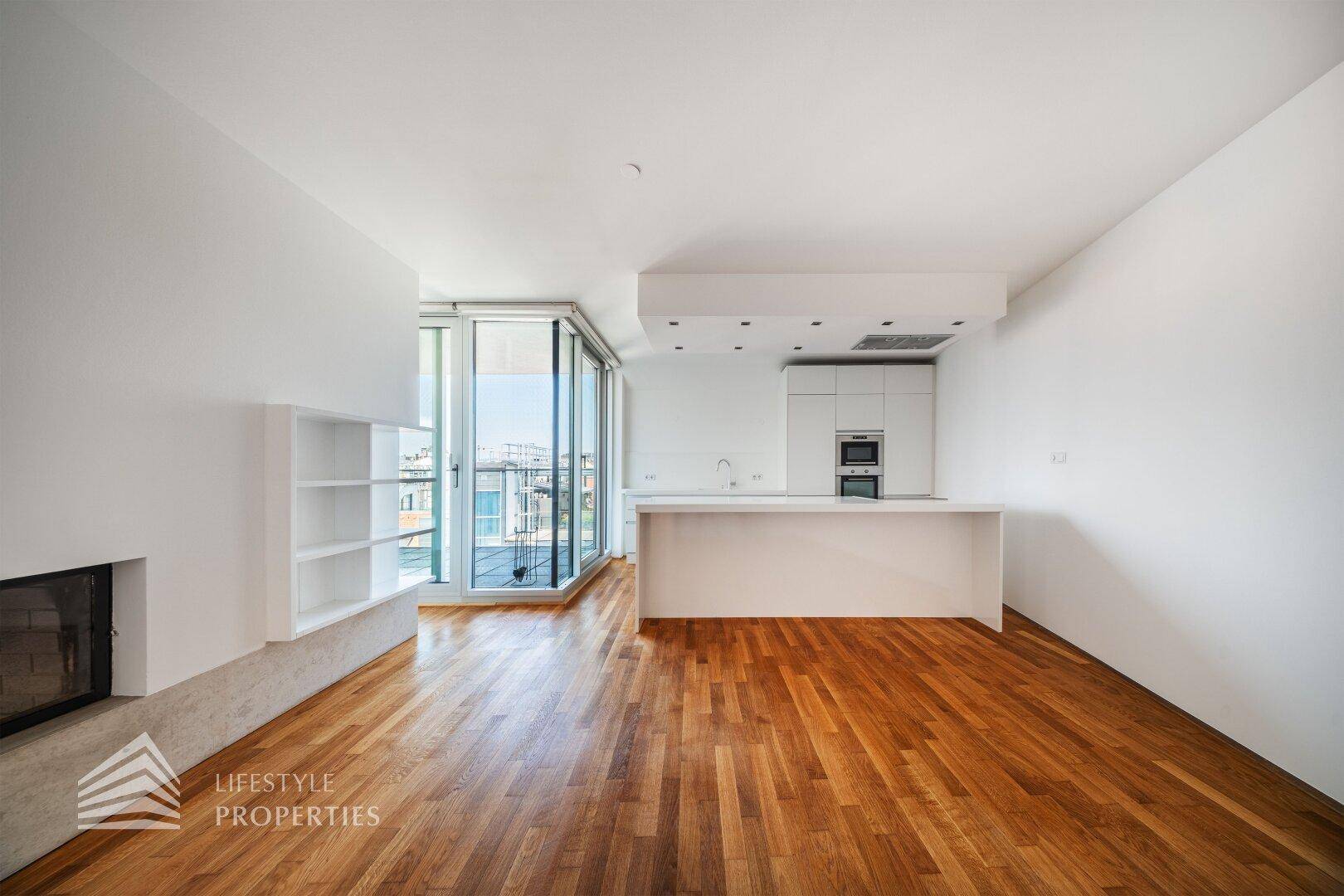 Geräumiger Wohnbereich mit Holzboden, integrierter Küche und Zugang zu einem Balkon.