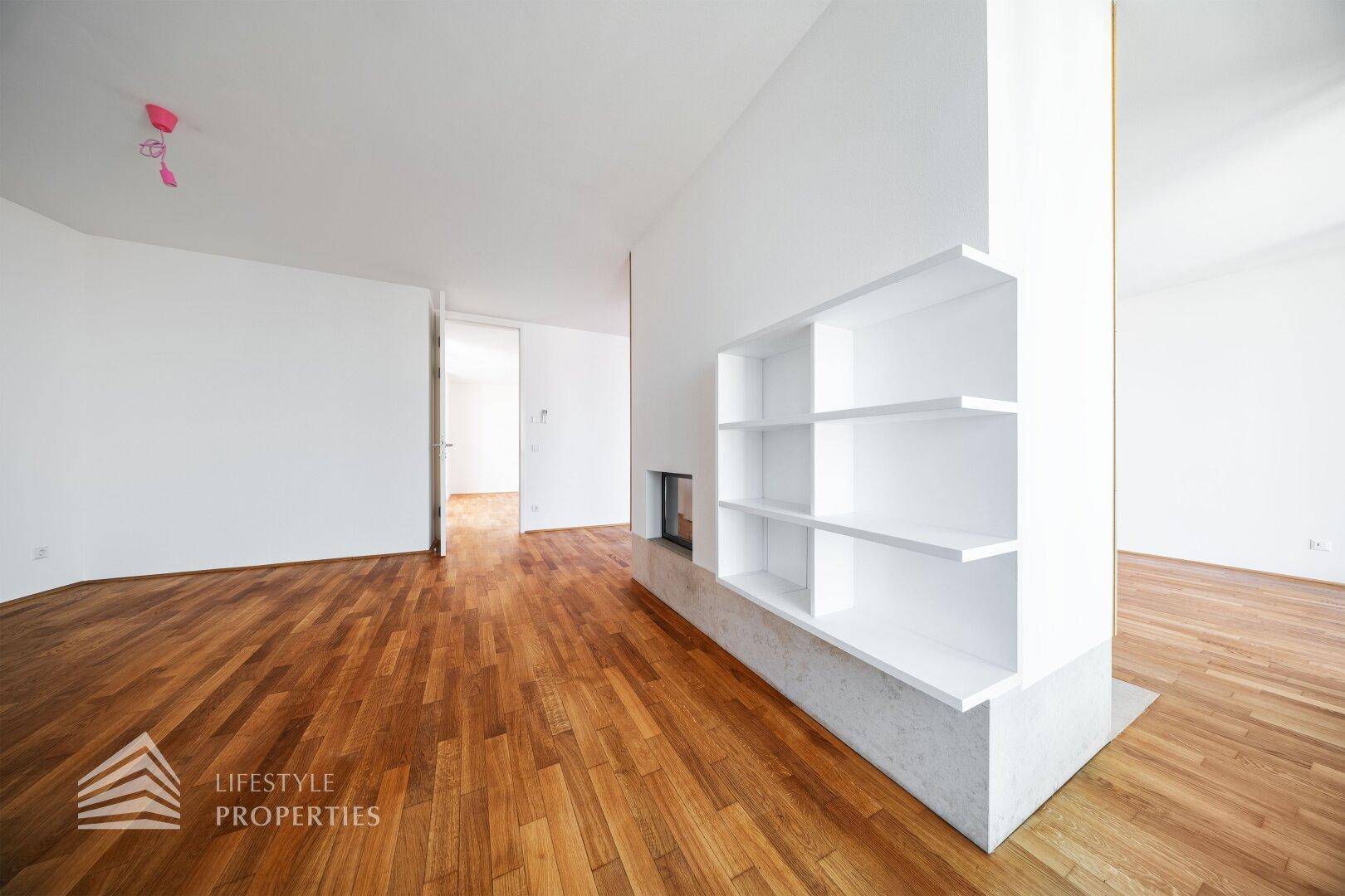 Heller Wohnbereich mit Holzboden, modernem Kamin und integrierten weißen Regalen.