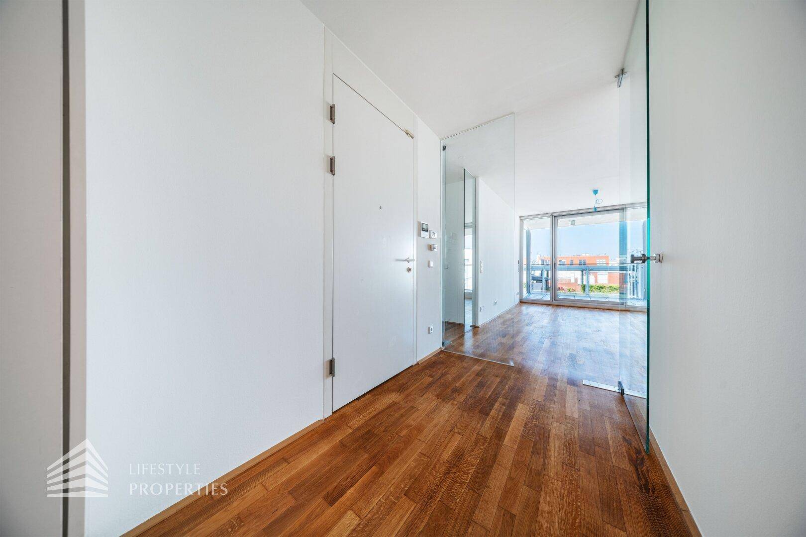 Heller Eingangsbereich mit Holzboden und einer modernen Glastür, die zum Wohnbereich führt.