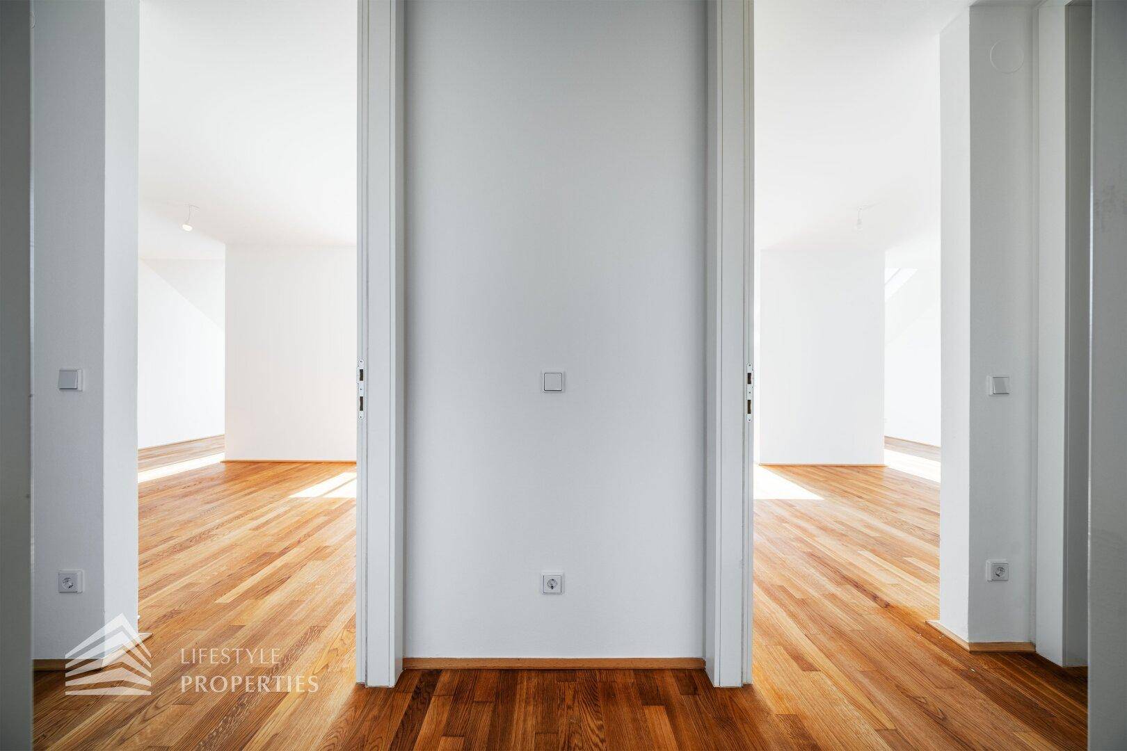 Heller Flur mit Holzboden, der zu weiteren leeren Räumen mit viel Tageslicht führt.