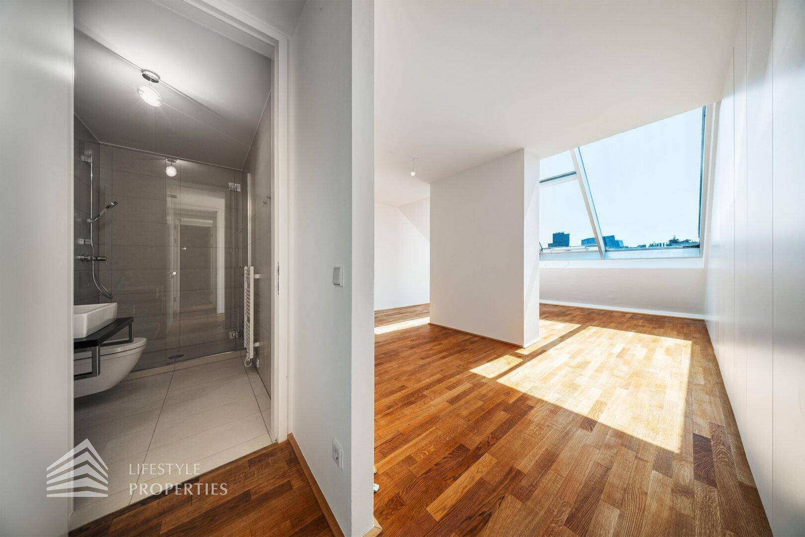Helles Dachgeschosszimmer mit Holzboden und direktem Zugang zu einem modernen Badezimmer.