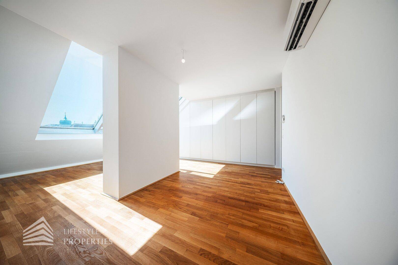 Dachgeschosszimmer mit Holzboden, Einbauschränken und schrägen Wänden mit Dachfenstern.