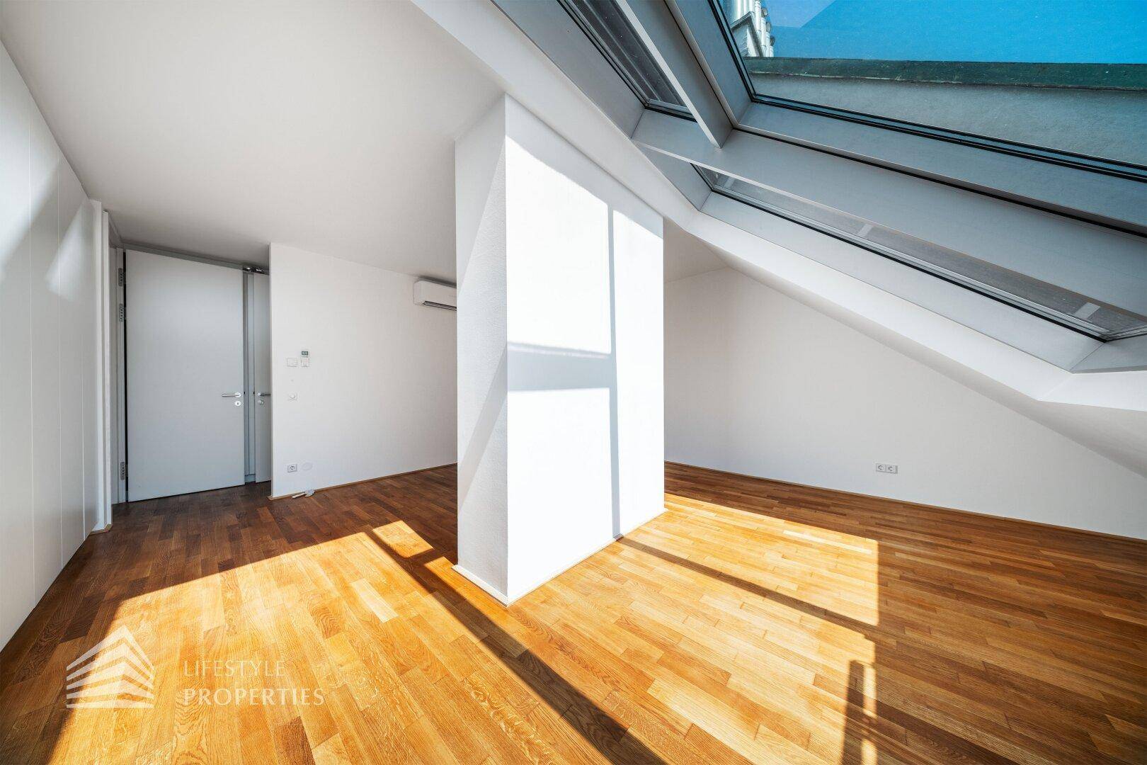 Helles Dachgeschosszimmer mit Holzboden und großen Dachfenstern, die viel Licht spenden.