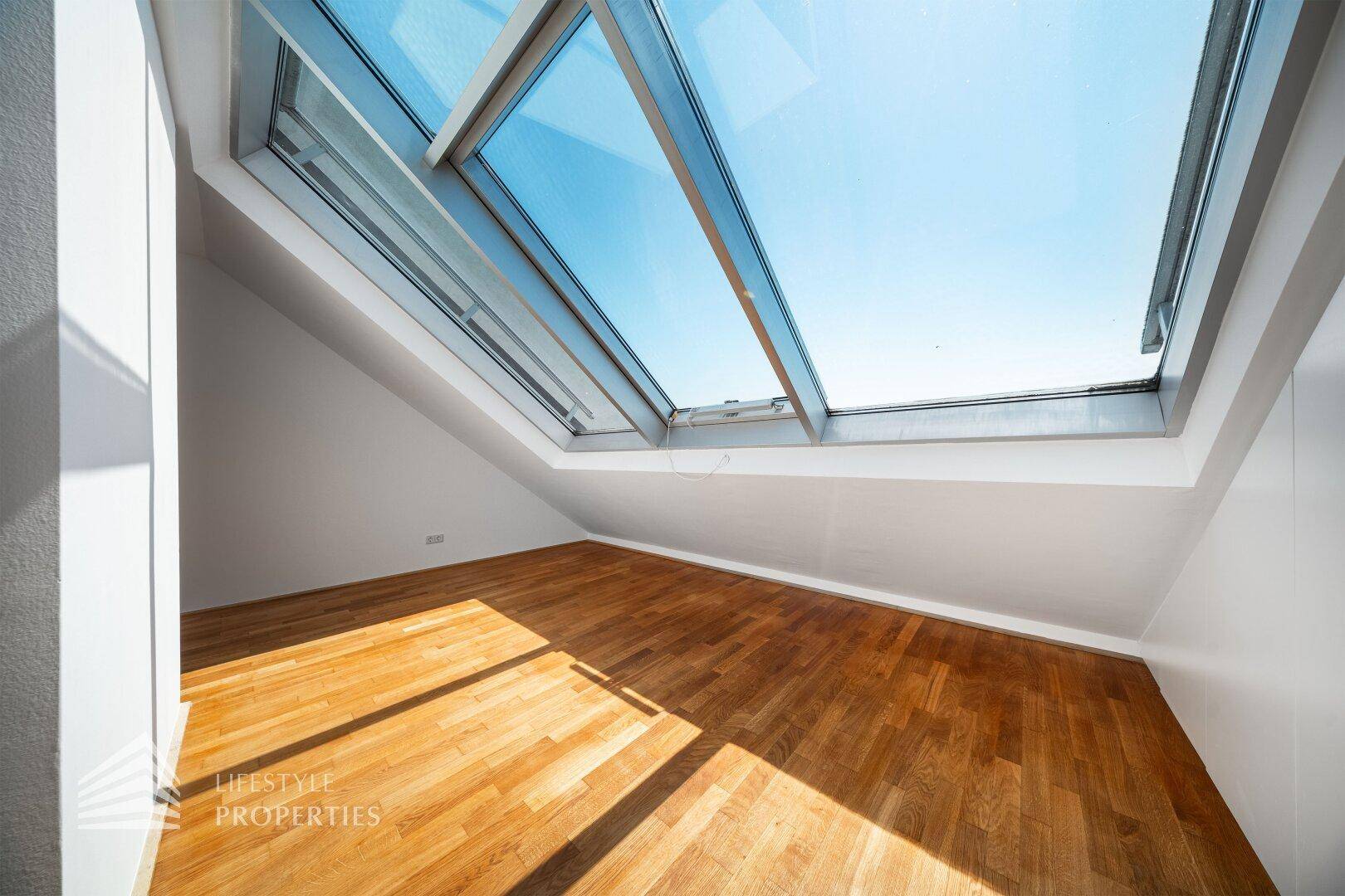 Geräumiges Dachgeschosszimmer mit Holzboden und beeindruckenden Dachfenstern für viel Tageslicht.