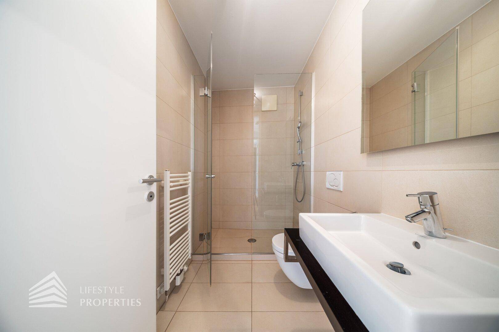 Helles Badezimmer mit beigen Fliesen, modernem Waschtisch und geräumiger begehbarer Dusche.
