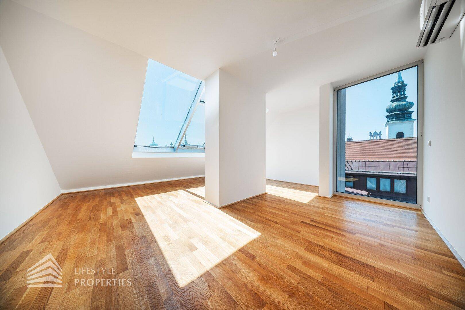Helles Dachgeschosszimmer mit Holzboden, Dachfenstern und einem vertikalen Fenster mit Stadtblick.