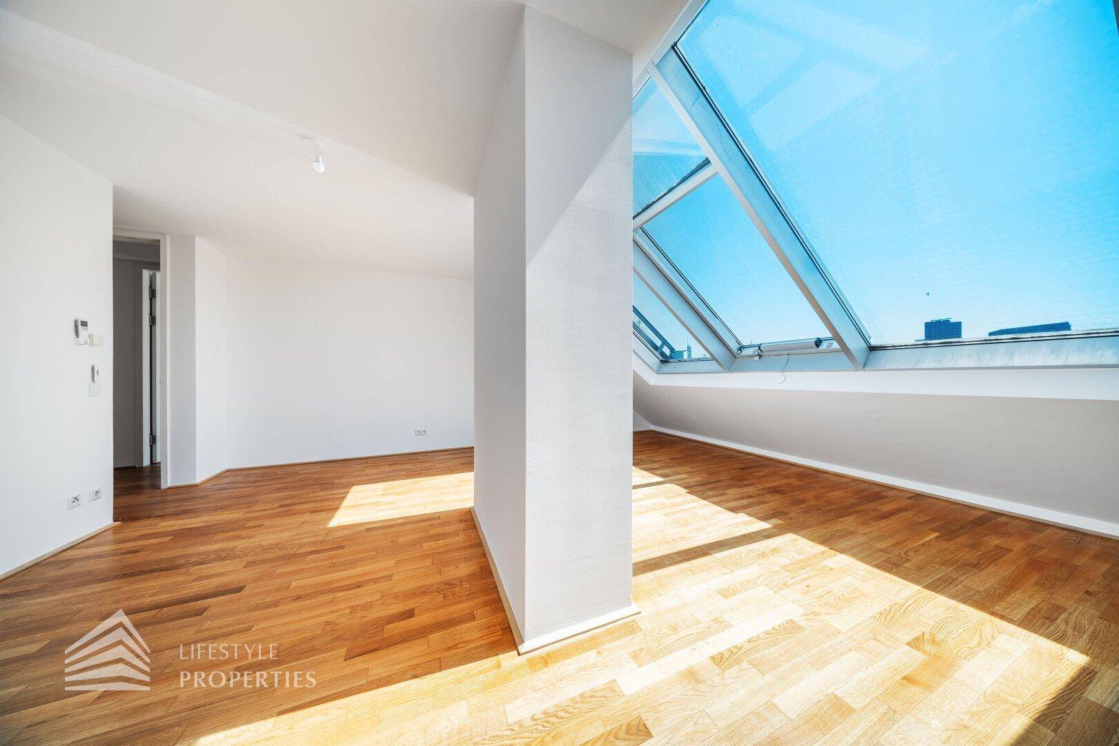 Dachgeschosszimmer mit Holzboden, schrägen Wänden und großen Dachfenstern für eine helle Atmosphäre.