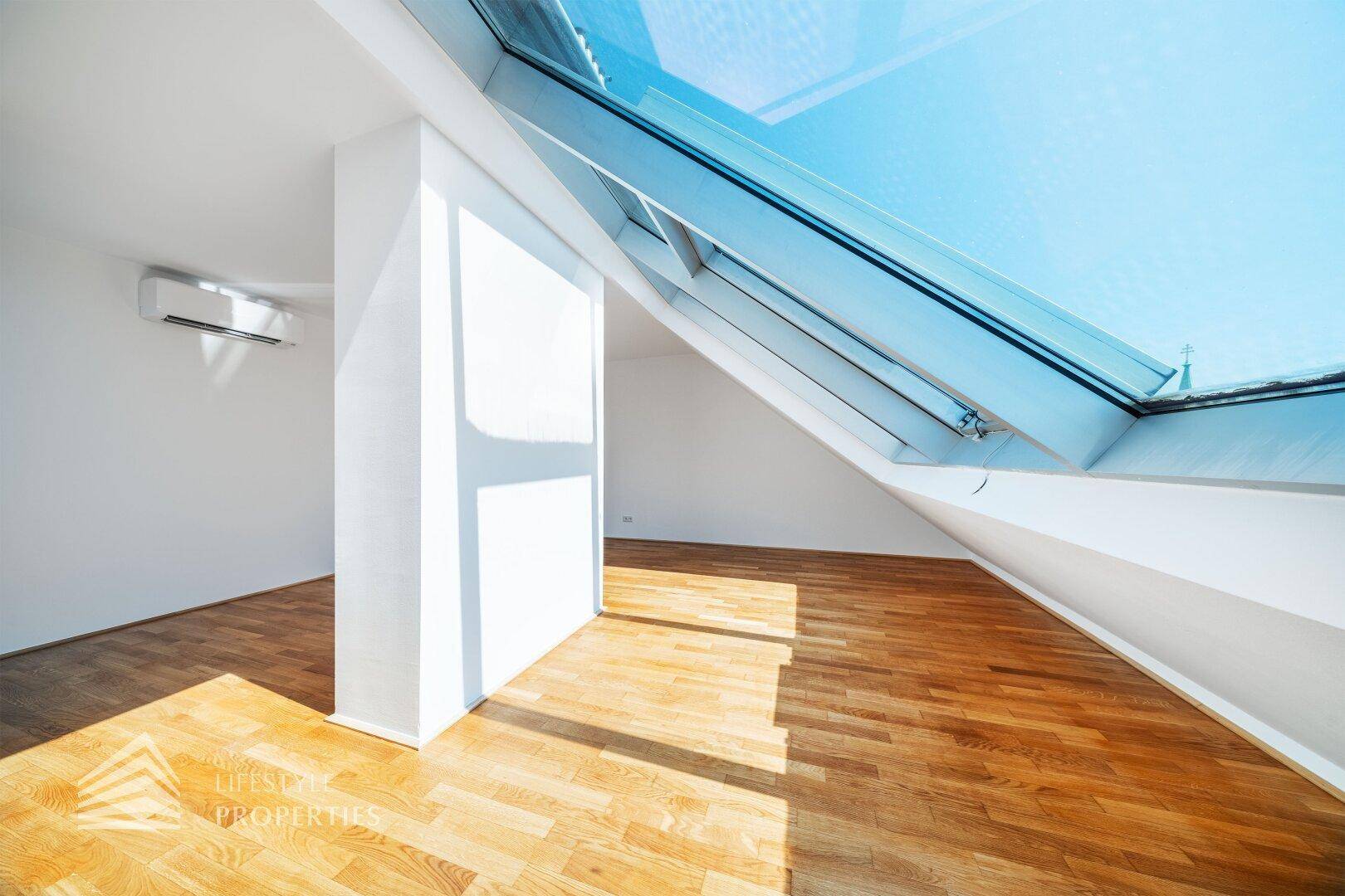 Geräumiges Dachgeschosszimmer mit Holzboden und großen Dachfenstern, die den Raum erhellen.