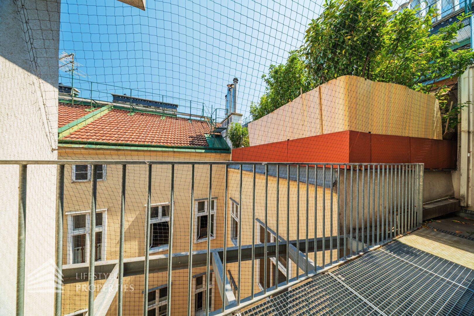 Kleiner Außenbereich mit Metallgeländer und Blick auf den Innenhof und die umliegenden Gebäude.