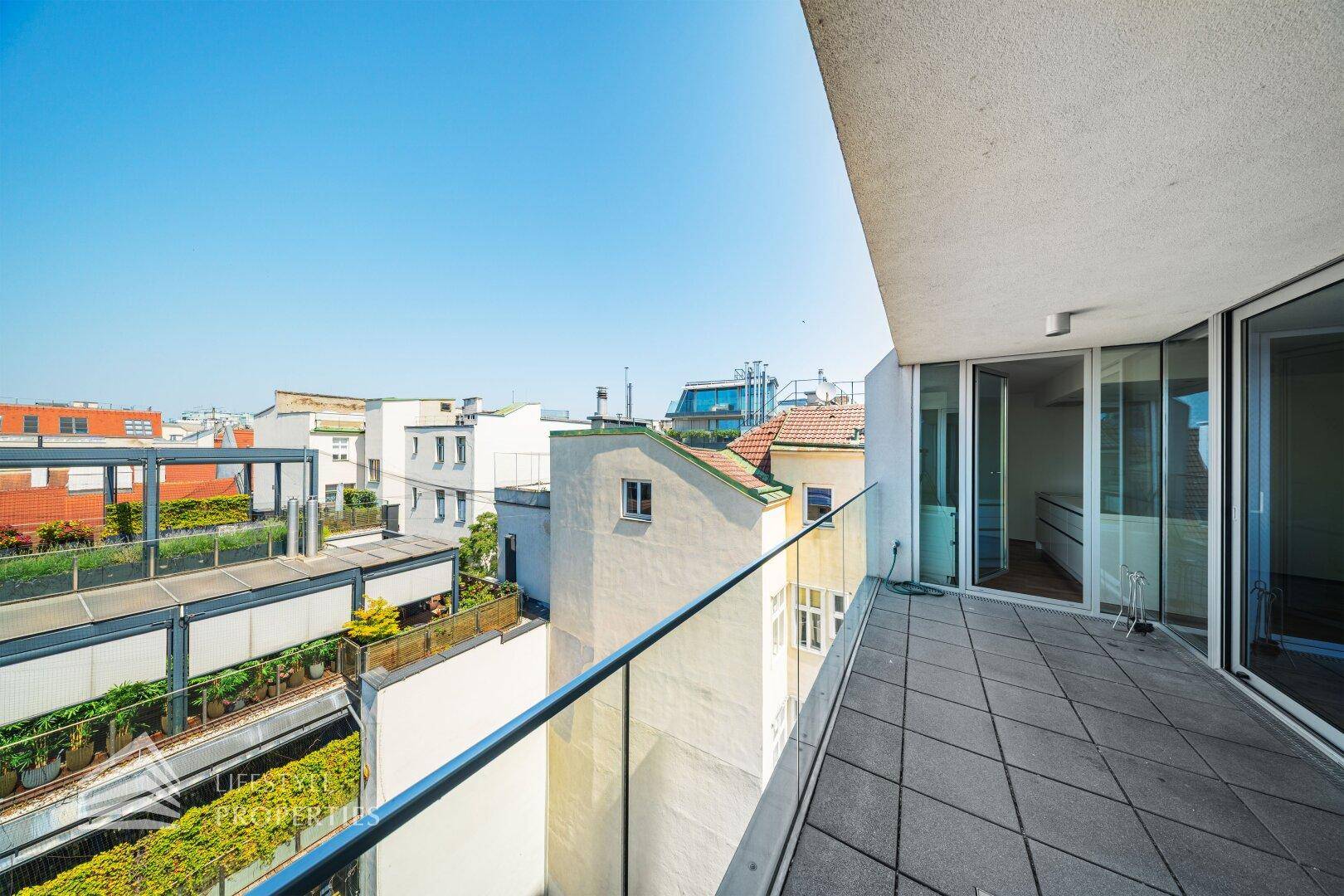 Heller Balkon mit moderner Glasbrüstung und Ausblick auf die umliegenden Gebäude und Dächer.
