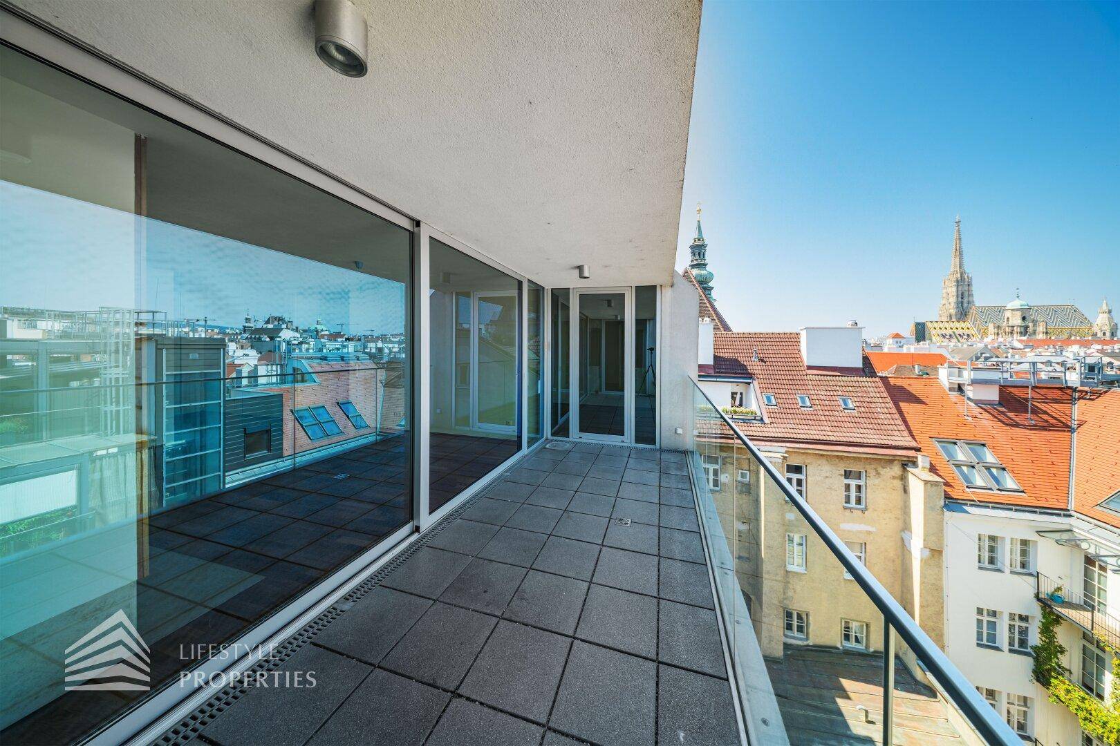 Geräumiger Balkon mit Glasgeländer und weitem Blick über die Stadt und den Stephansdom.