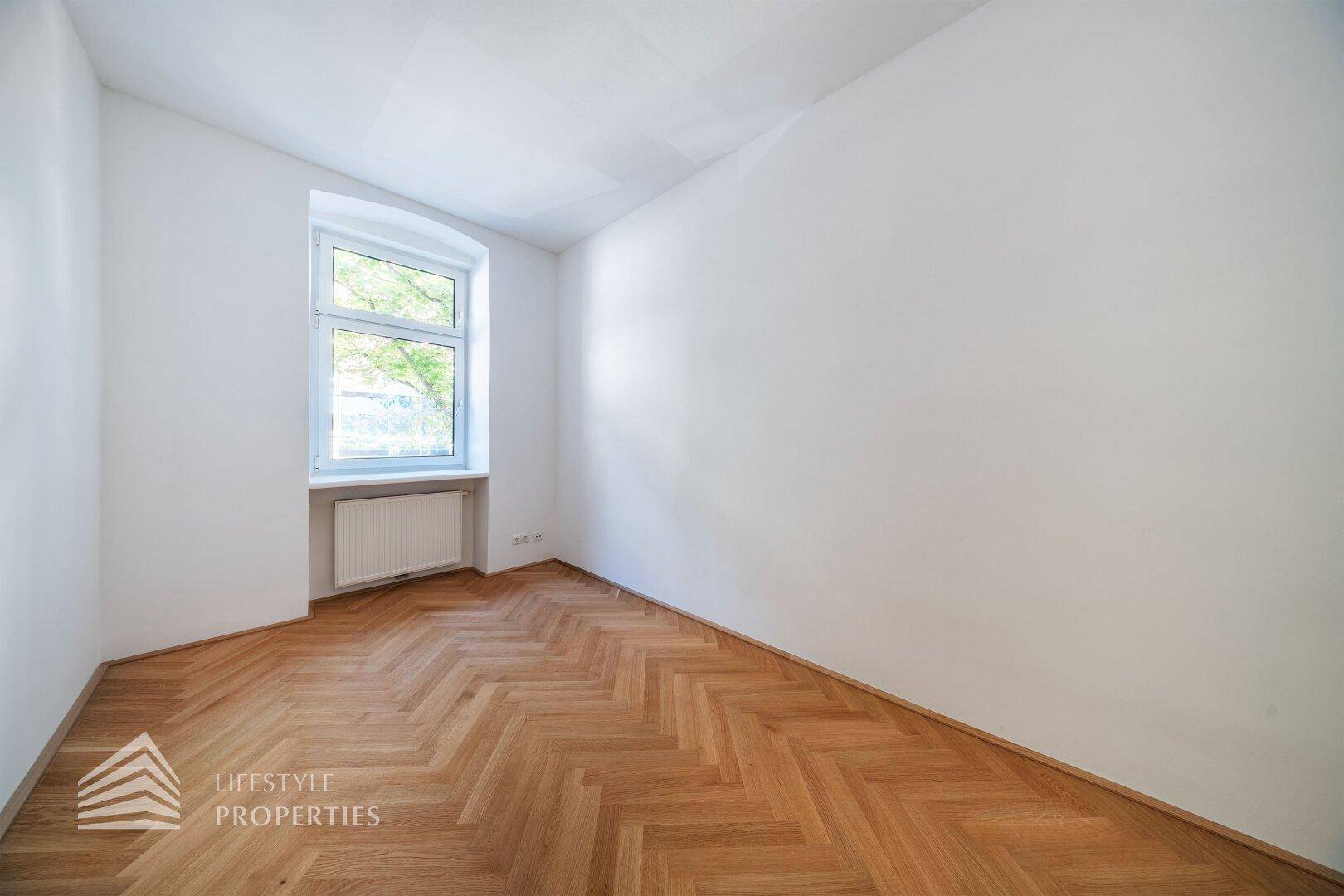 Ruhiges Zimmer mit Fischgrätparkett und einem Fenster, das viel natürliches Licht spendet.