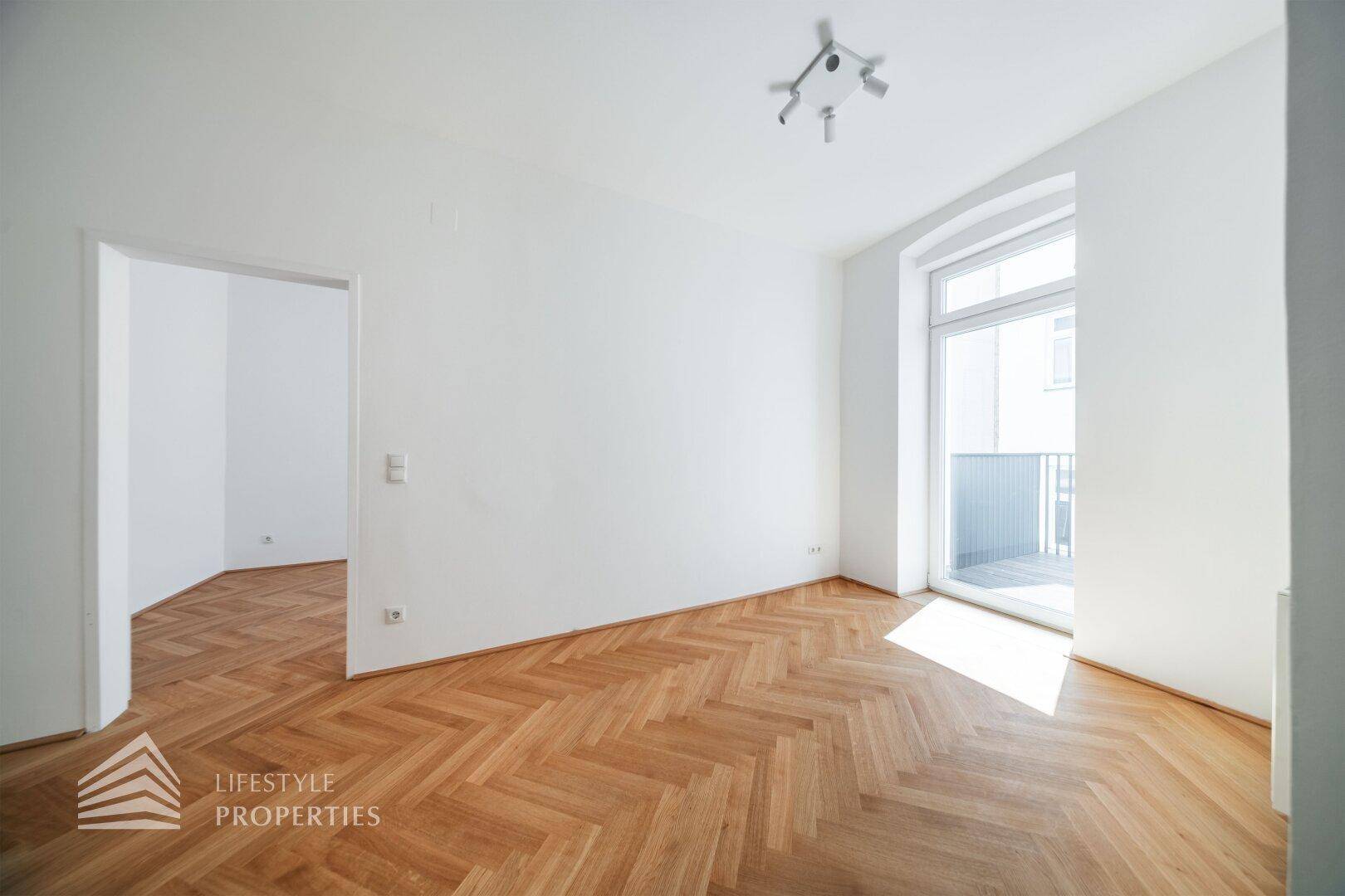 Heller Raum mit Fischgrätparkett und Zugang zu einem Balkon, ideal für sonnige Tage.