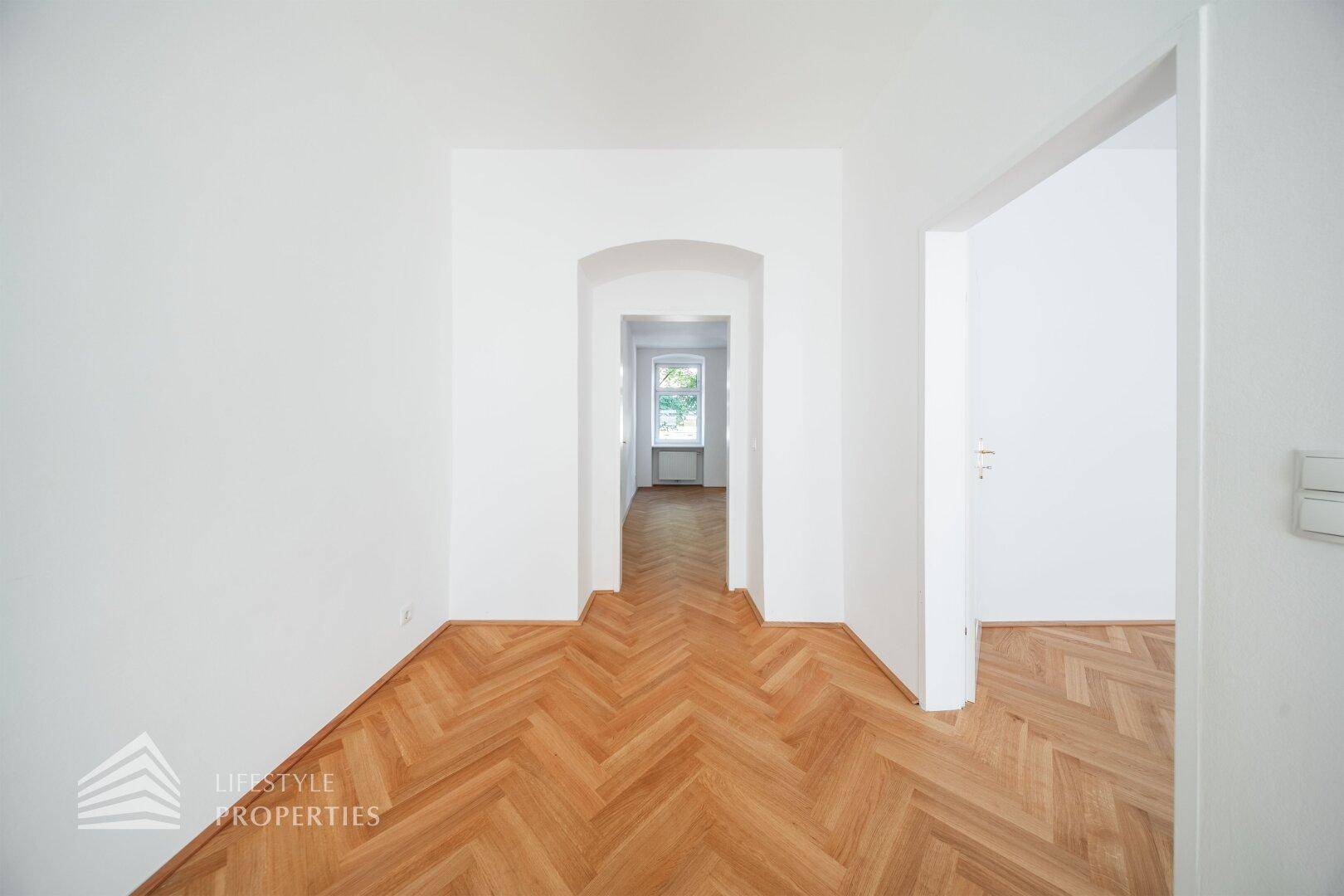 Langer Flur mit Fischgrätparkett, der zu weiteren hellen Zimmern der Wohnung führt.