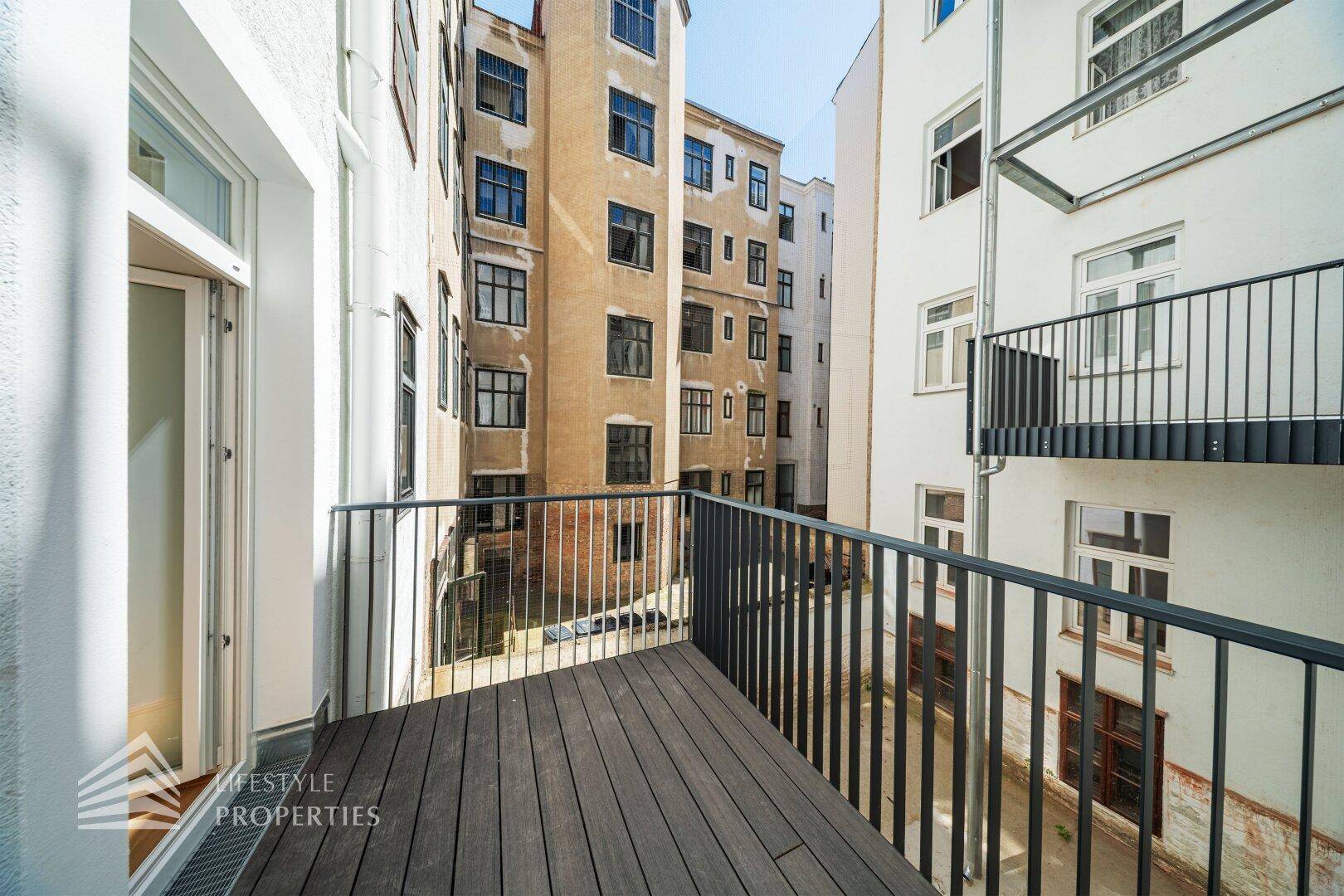 Balkon mit Holzboden und Metallgeländer, bietet Blick auf den Innenhof des Gebäudes.