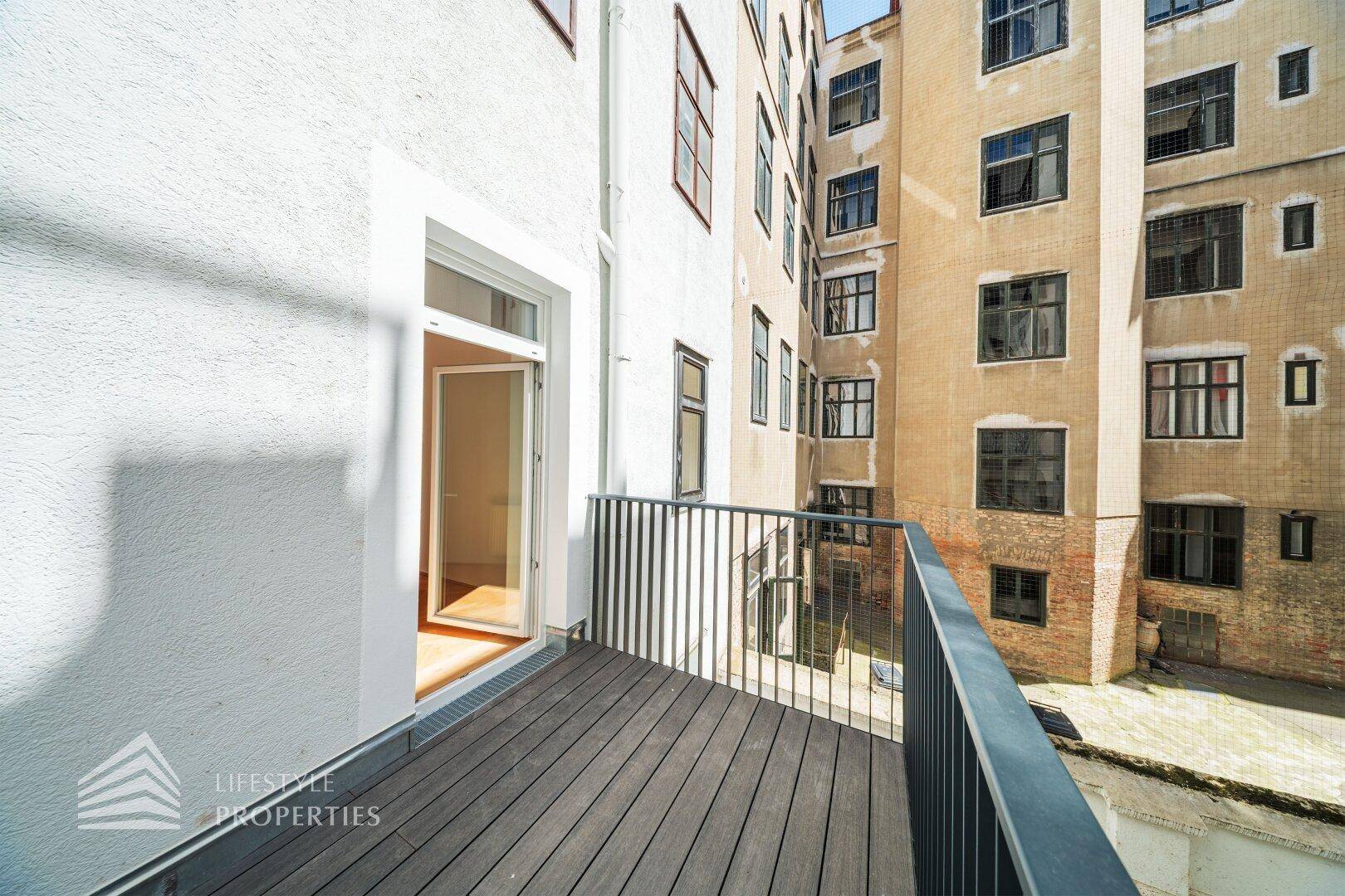 Schmaler Balkon mit Holzboden und Blick auf die umliegenden Gebäude im Innenhof.