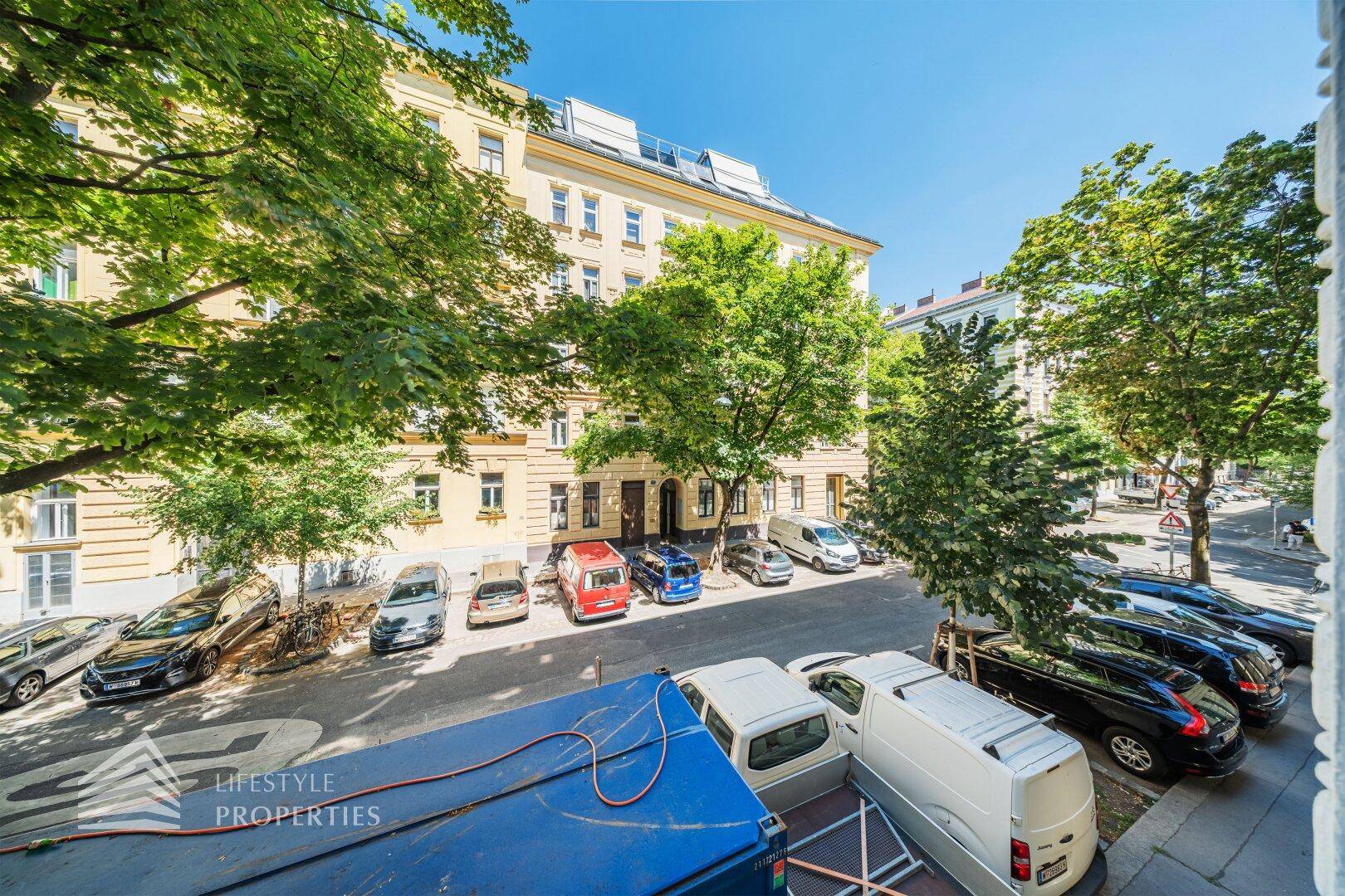 Panoramablick auf eine städtische Straße mit parkenden Fahrzeugen und historischen Gebäuden.