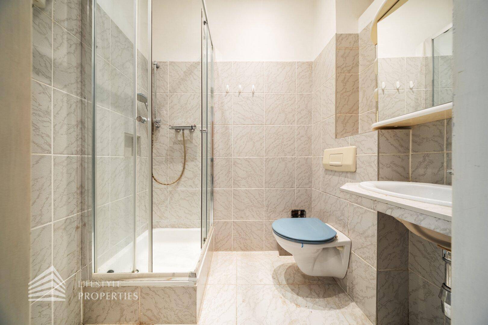 Funktionales Badezimmer mit Duschkabine, Wand-WC, Waschbecken und hellen Fliesen an Wänden und Boden.
