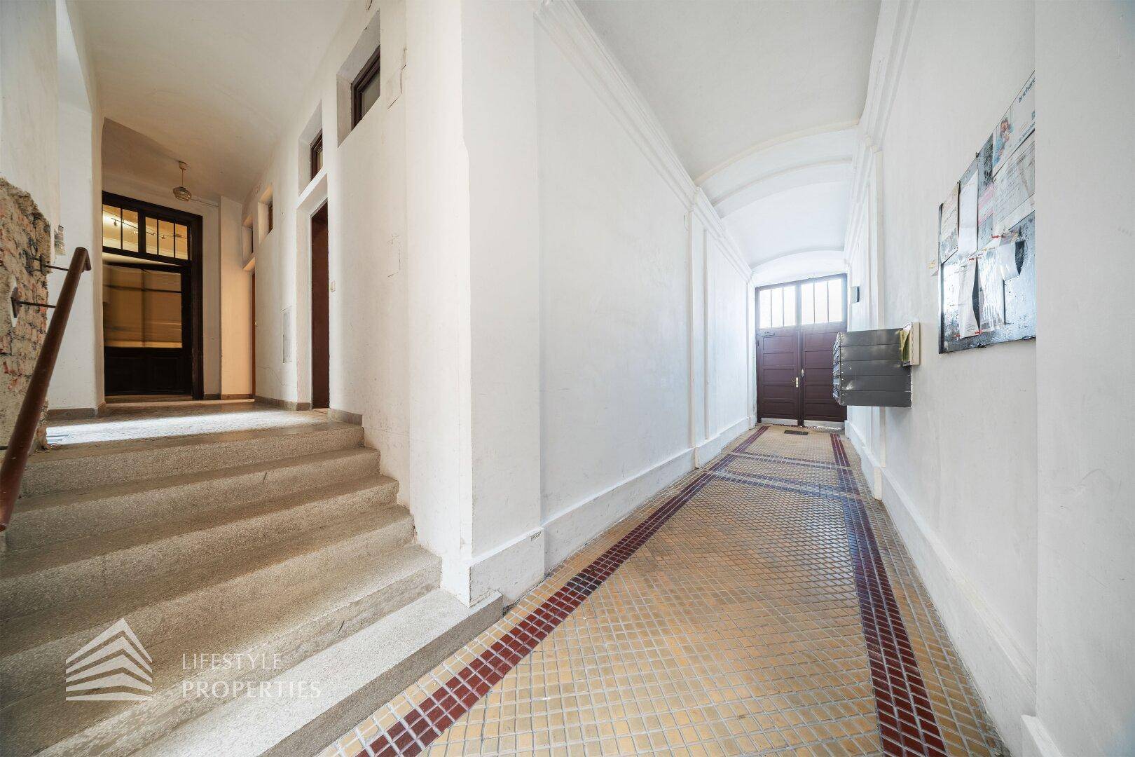 Historischer Eingangsbereich mit Treppe, gemustertem Fliesenboden und hohen Decken in einem Altbau.