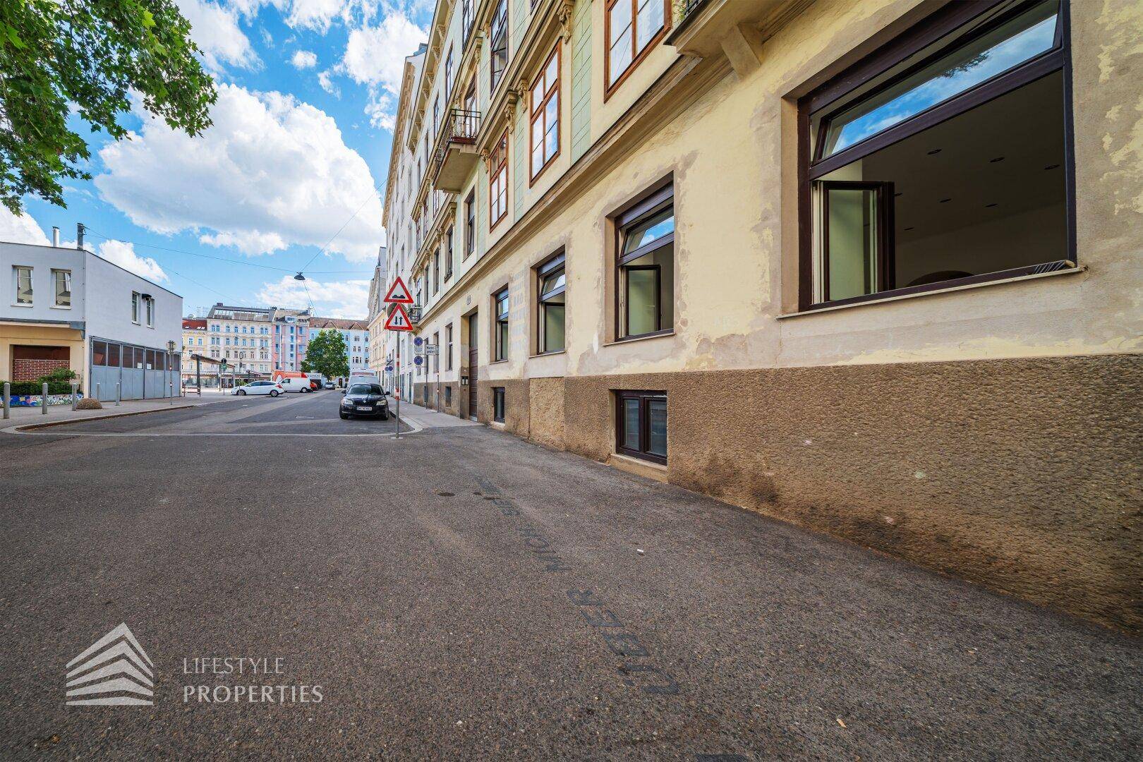 Seitenansicht eines Gebäudes an einer städtischen Straße mit parkenden Autos und einem klaren Himmel.