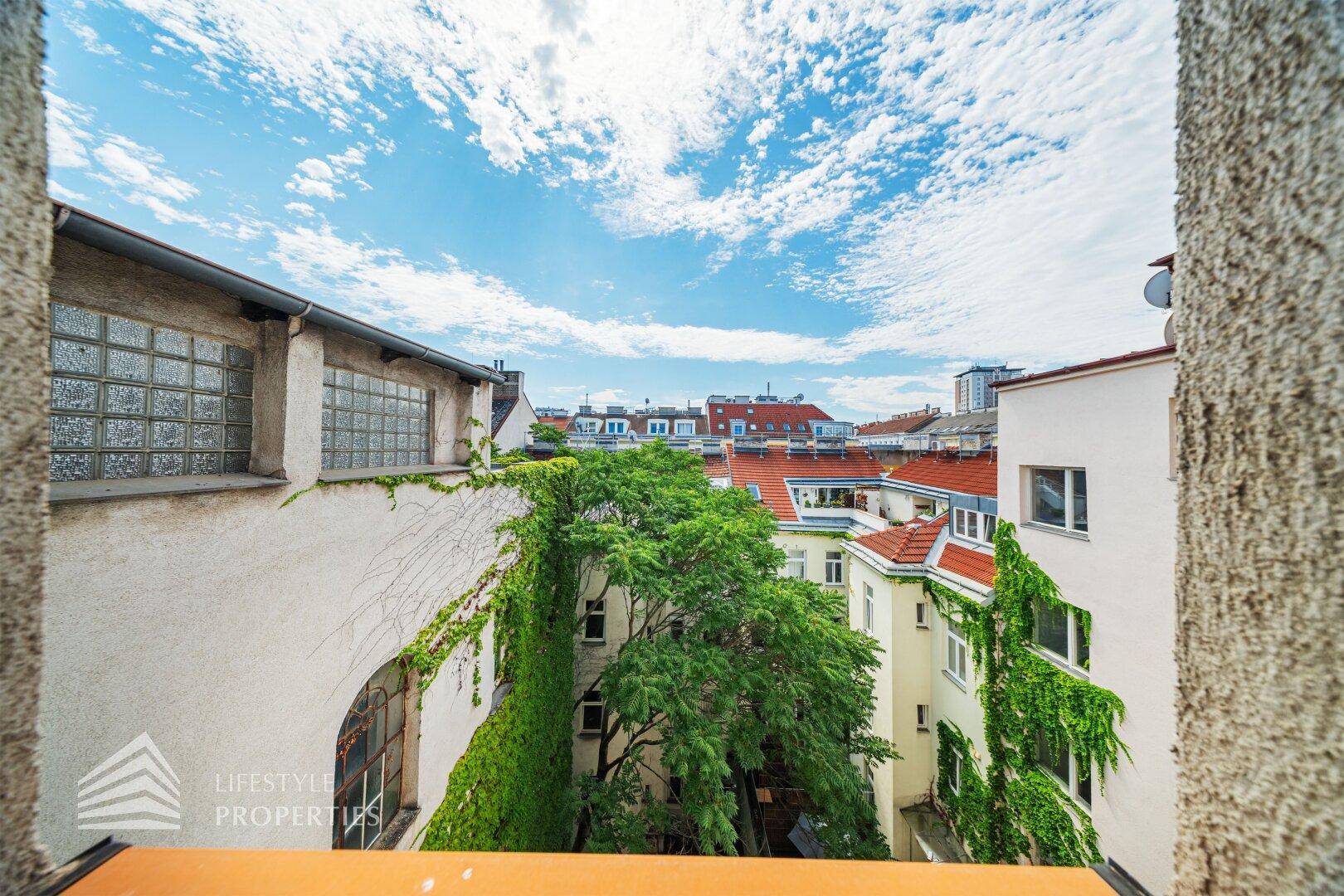 Blick über begrünte Innenhöfe und Dächer mit viel Grün und blauem Himmel.