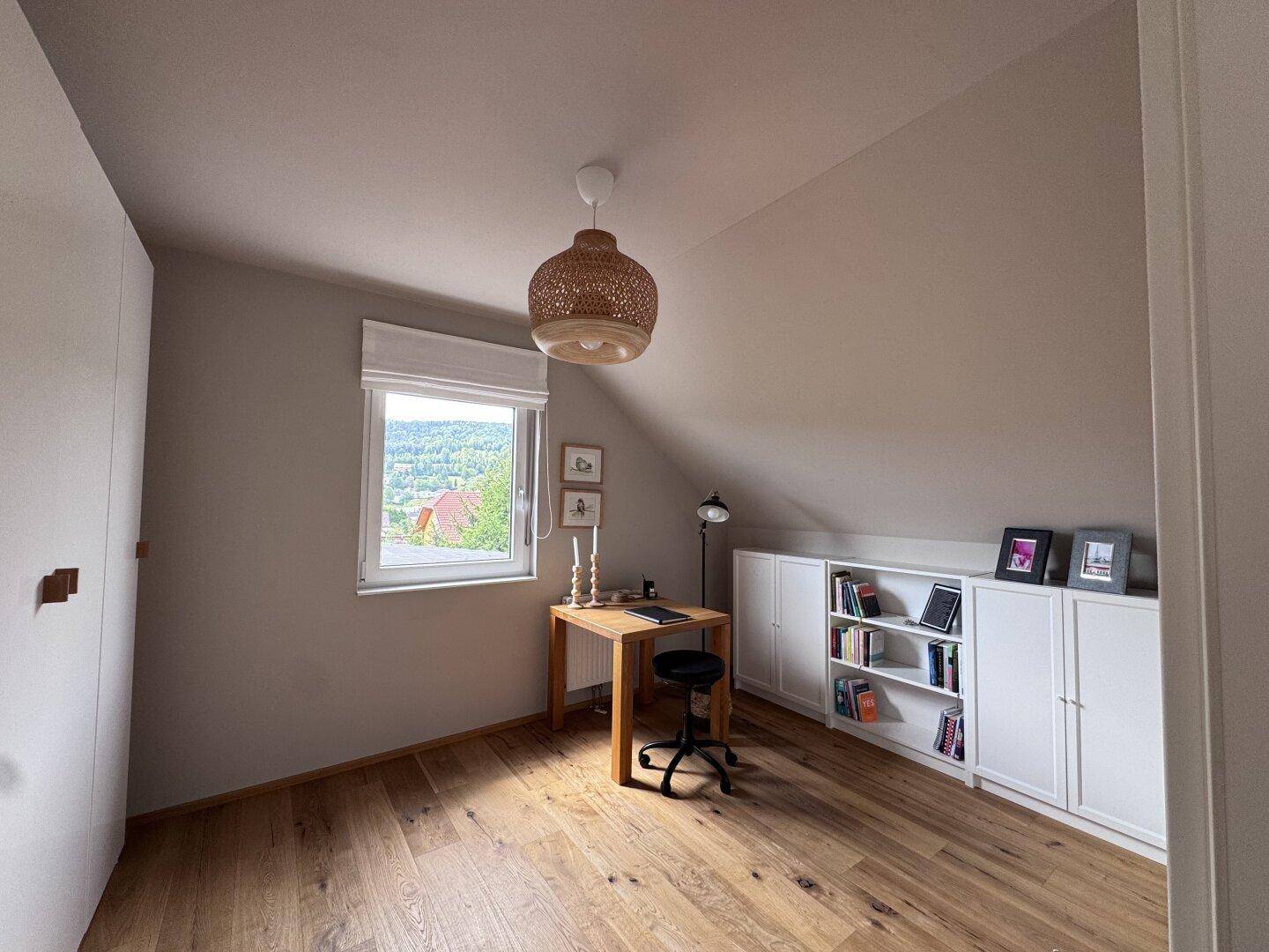 Arbeitszimmer mit Holzboden, Schreibtisch, Fenster und Blick auf die Landschaft.
