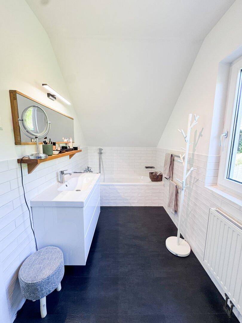 Modernes Badezimmer mit Badewanne, Waschtisch, dunklem Boden und Dachschräge.