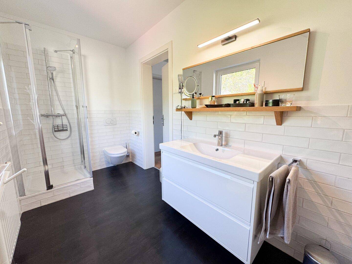 Modernes Badezimmer mit Duschkabine, Waschtisch, WC und dunklem Fliesenboden.