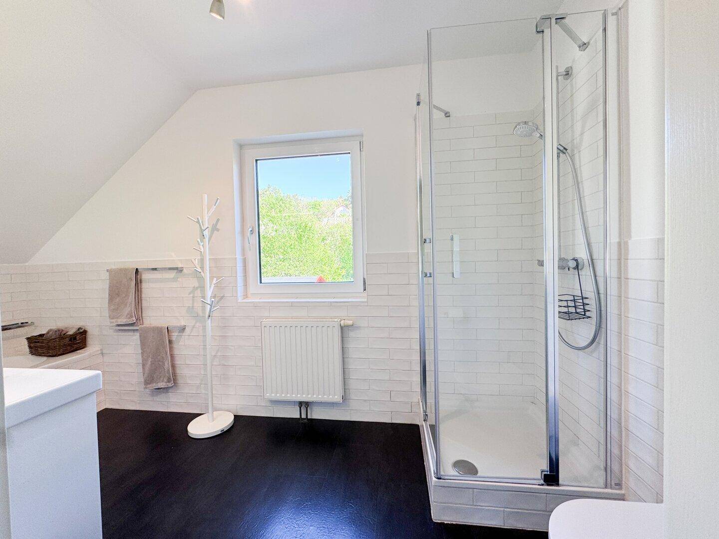 Modernes Badezimmer mit Duschkabine, Fenster, dunklem Boden und Dachschräge.