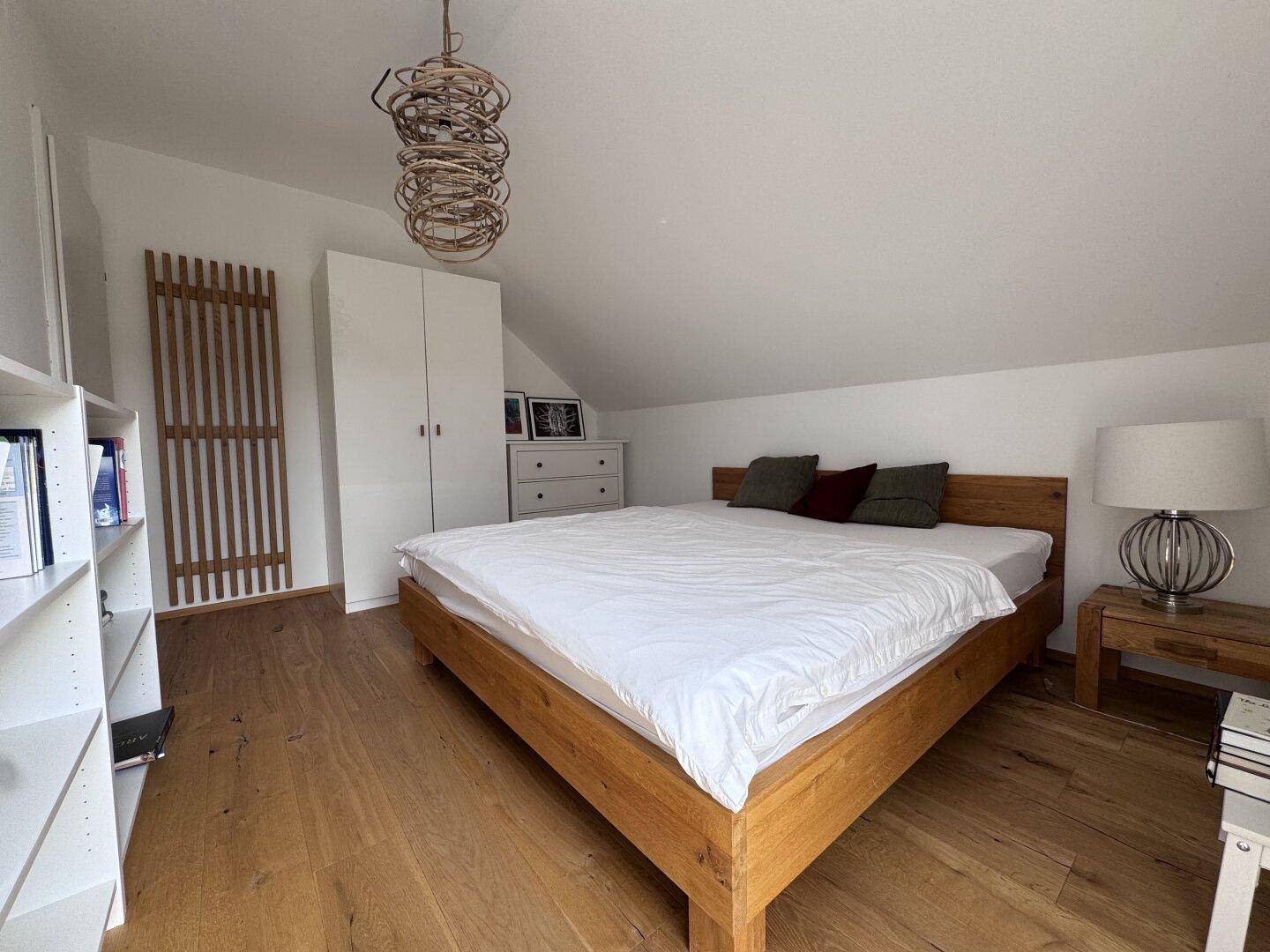 Gemütliches Schlafzimmer mit Holzbett, Holzboden, weißem Kleiderschrank und Dachschräge.