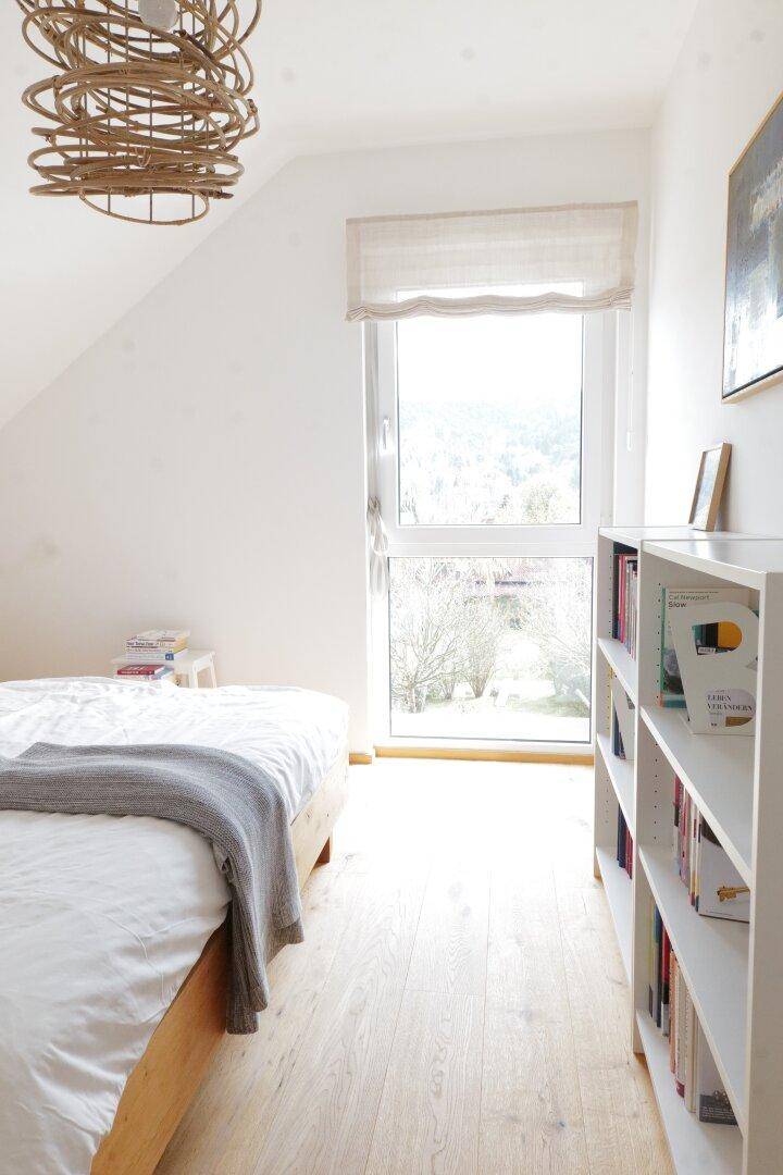 Lichtdurchflutetes Schlafzimmer mit Holzboden, Bücherregal und großem Fenster.